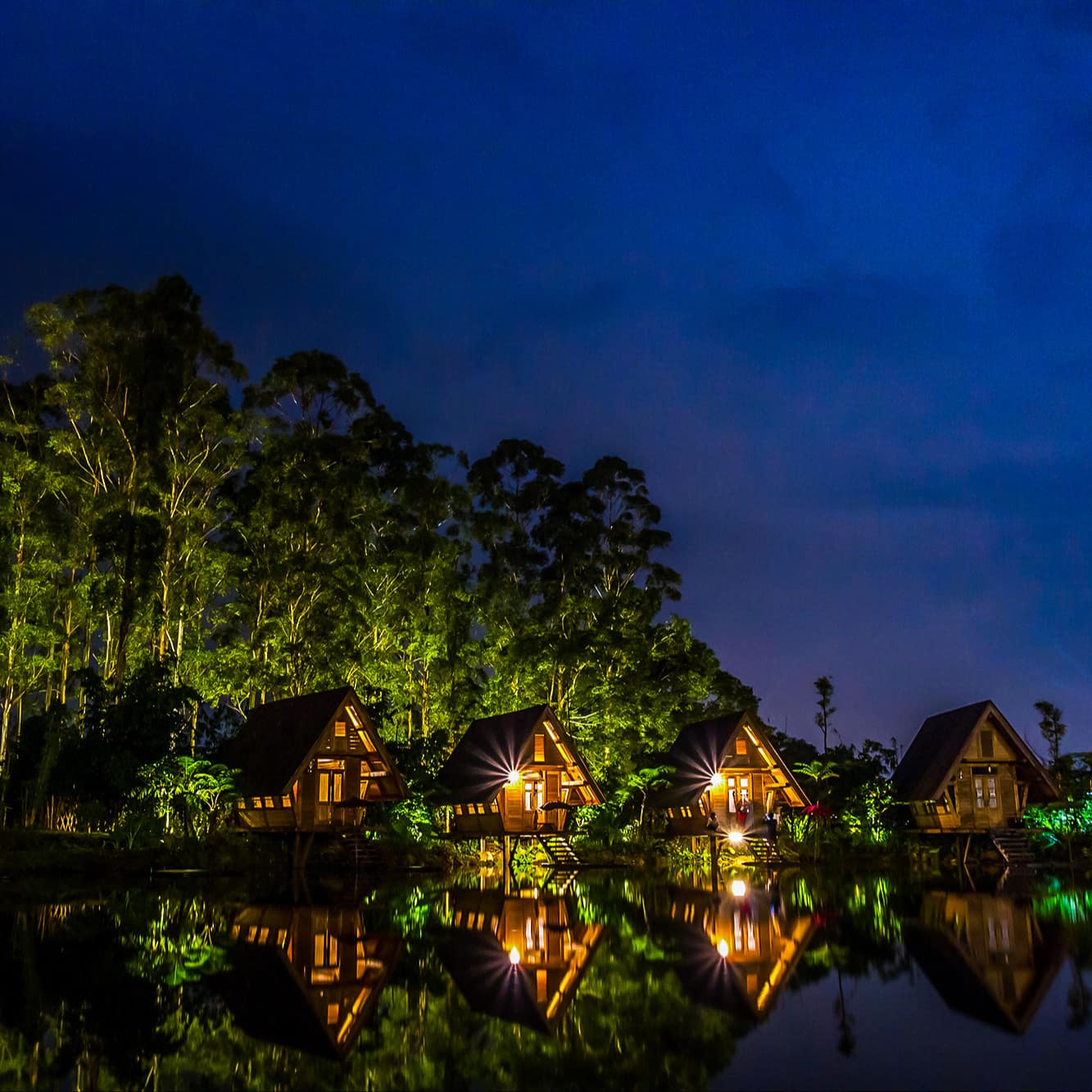 Bali waterfront villas at night lit up and casting reflections on the water and light on the trees in the background