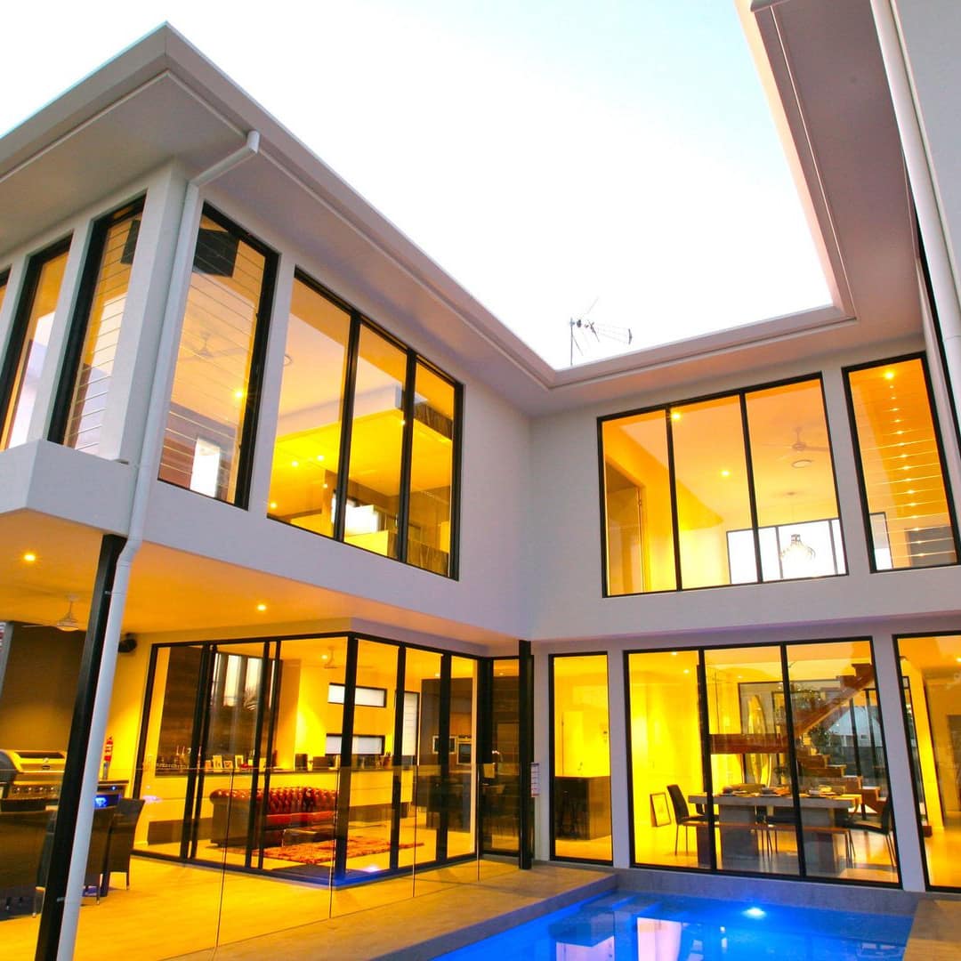 A modern two-story home with white siding, floor to ceiling windows, ground floor patio space, and a private pool.