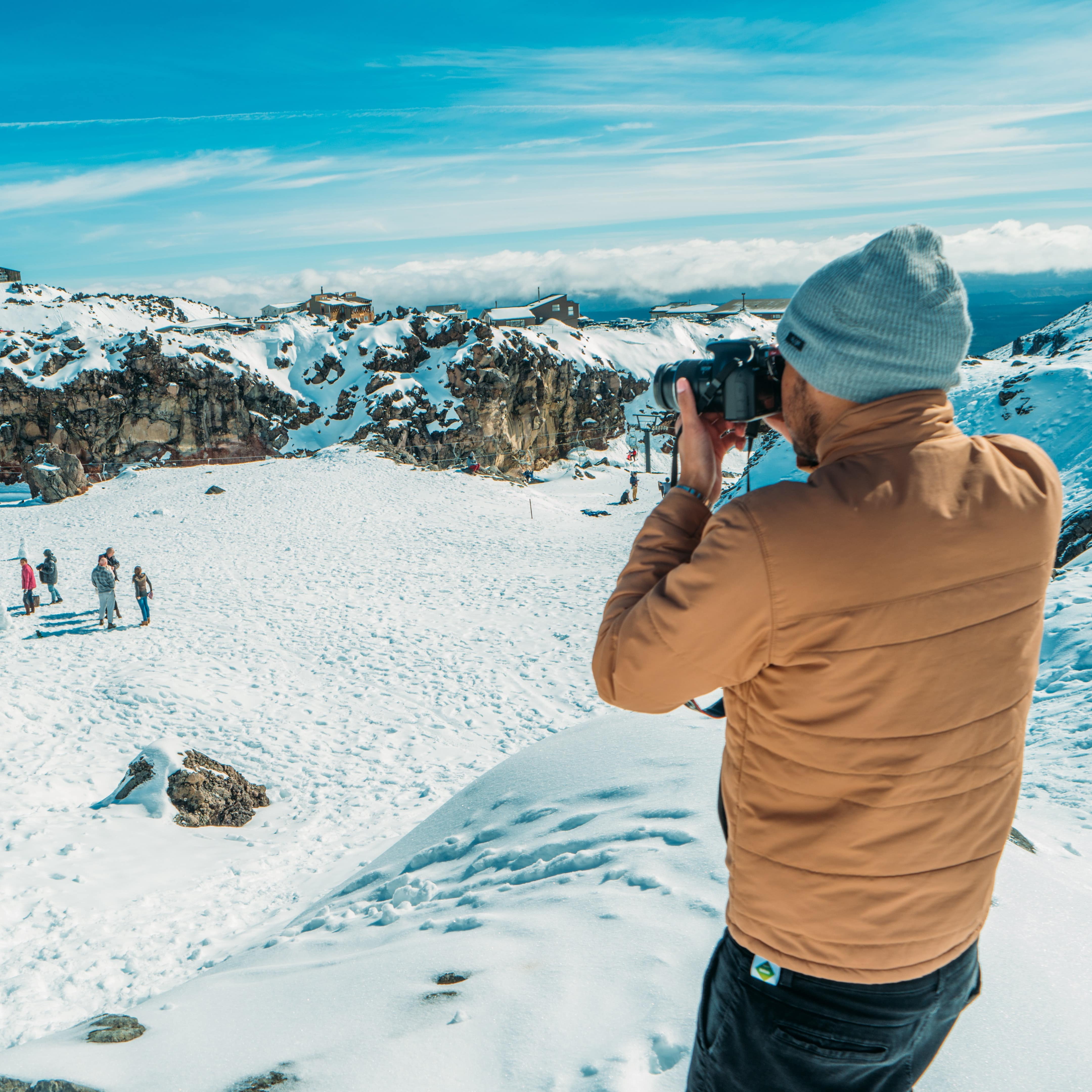 Man standing on a hill taking photos of skiers in the distance on a snowy mountainside