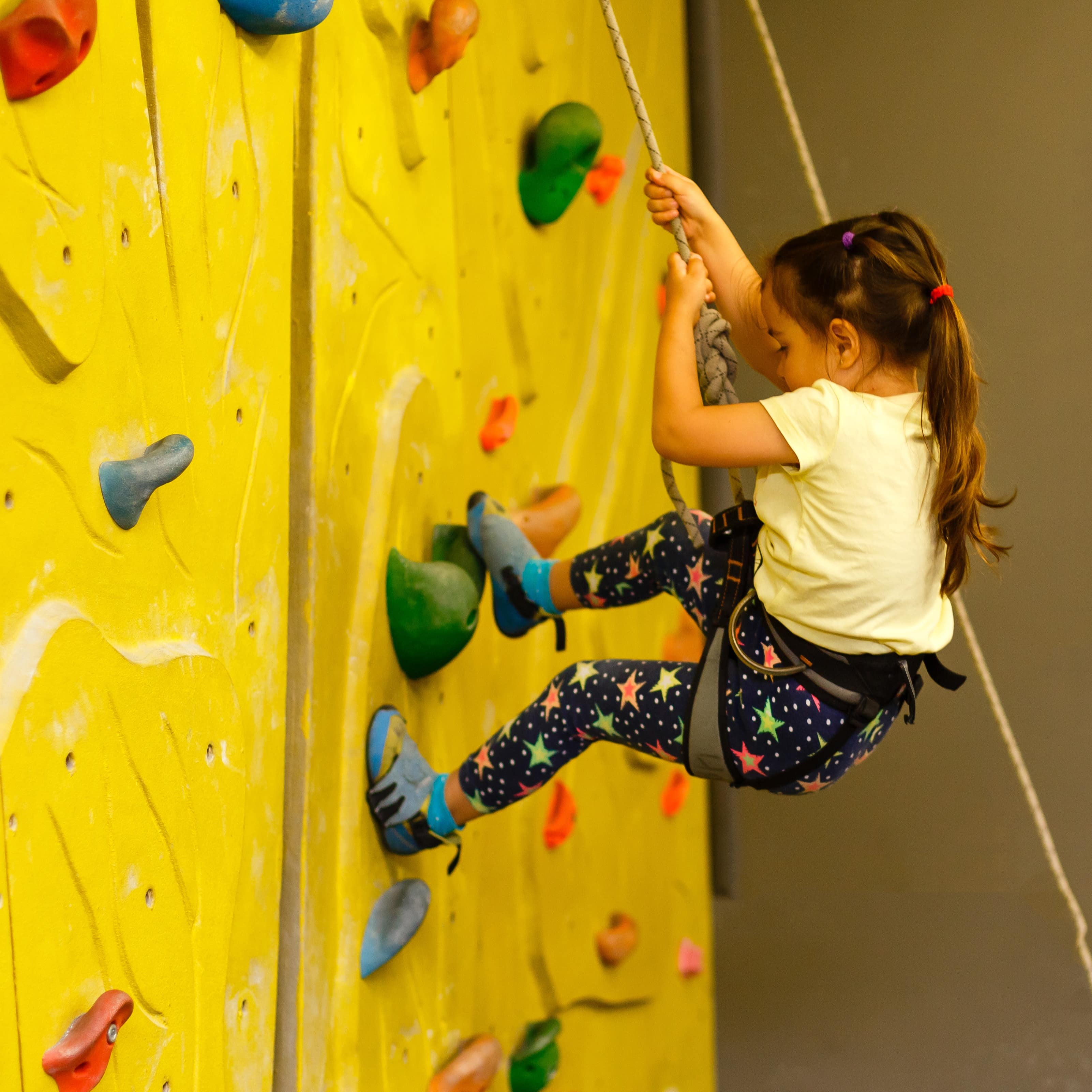 A little girl climbing a yellow rock wall indoors