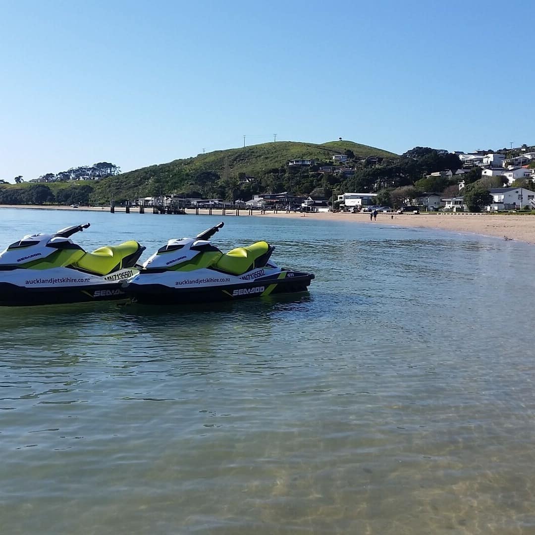 Two jetskis in the water at Maraetai beach with a view of beach houses in the background