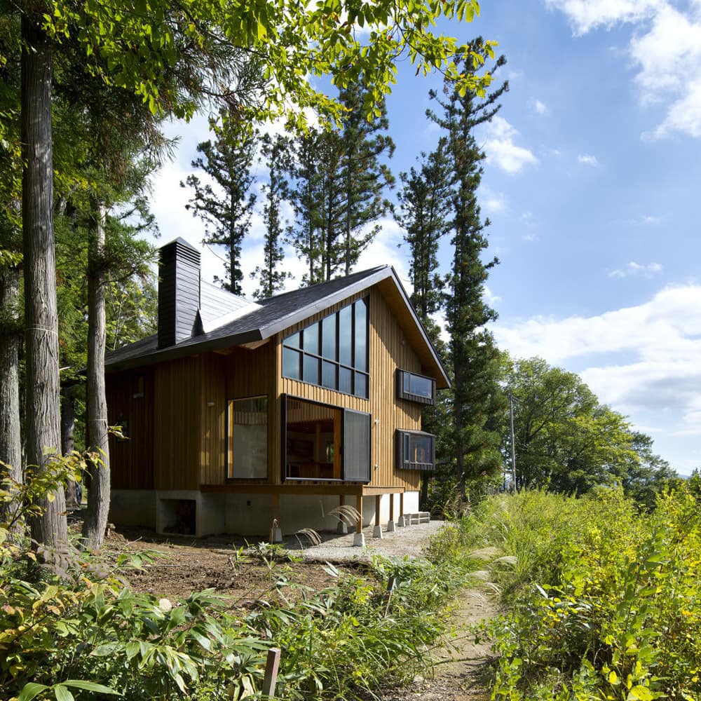 View of a modern two-story wood cabin with tall windows, overlooking mountainous landscape.