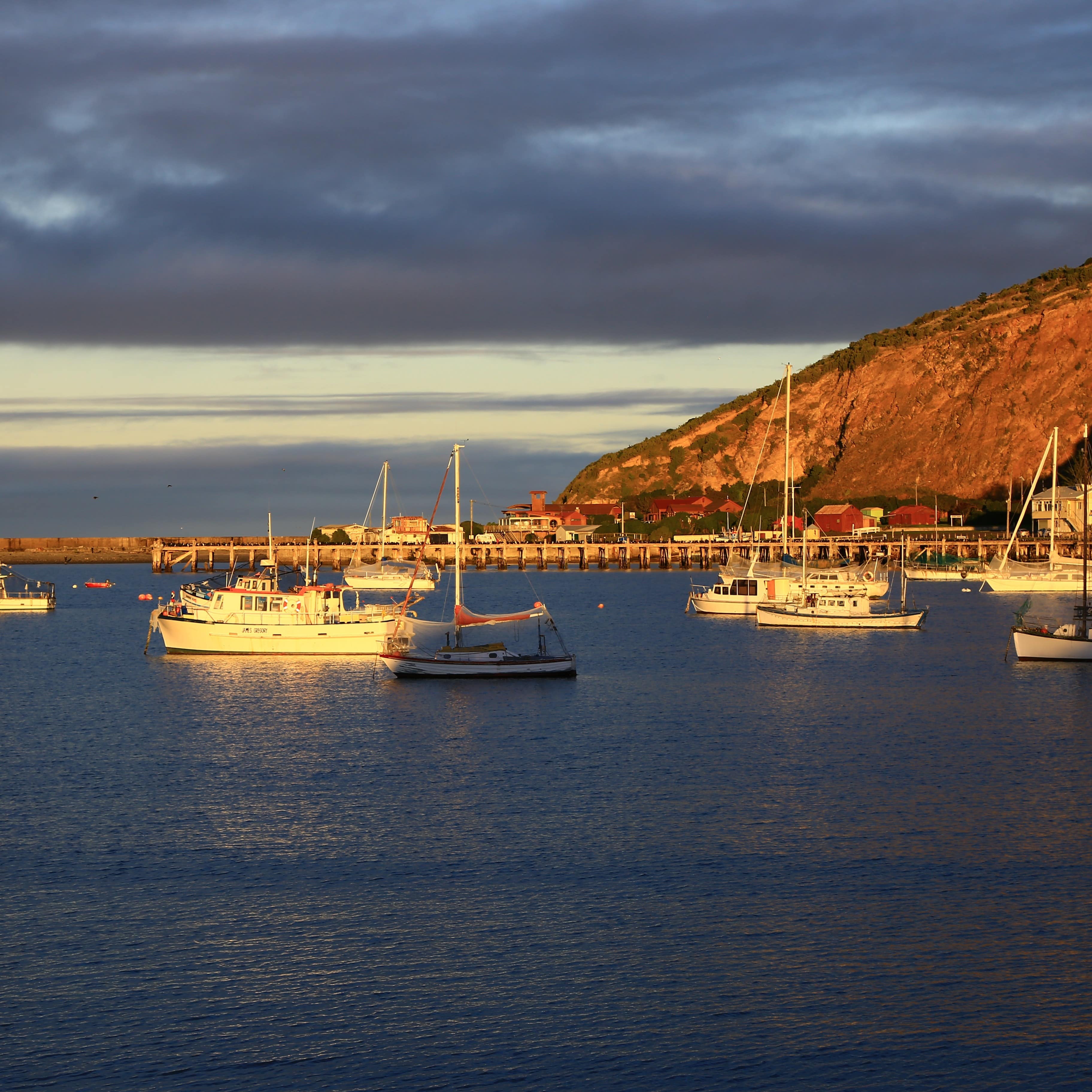 Boats in the bay with a view of the jetty and mountain