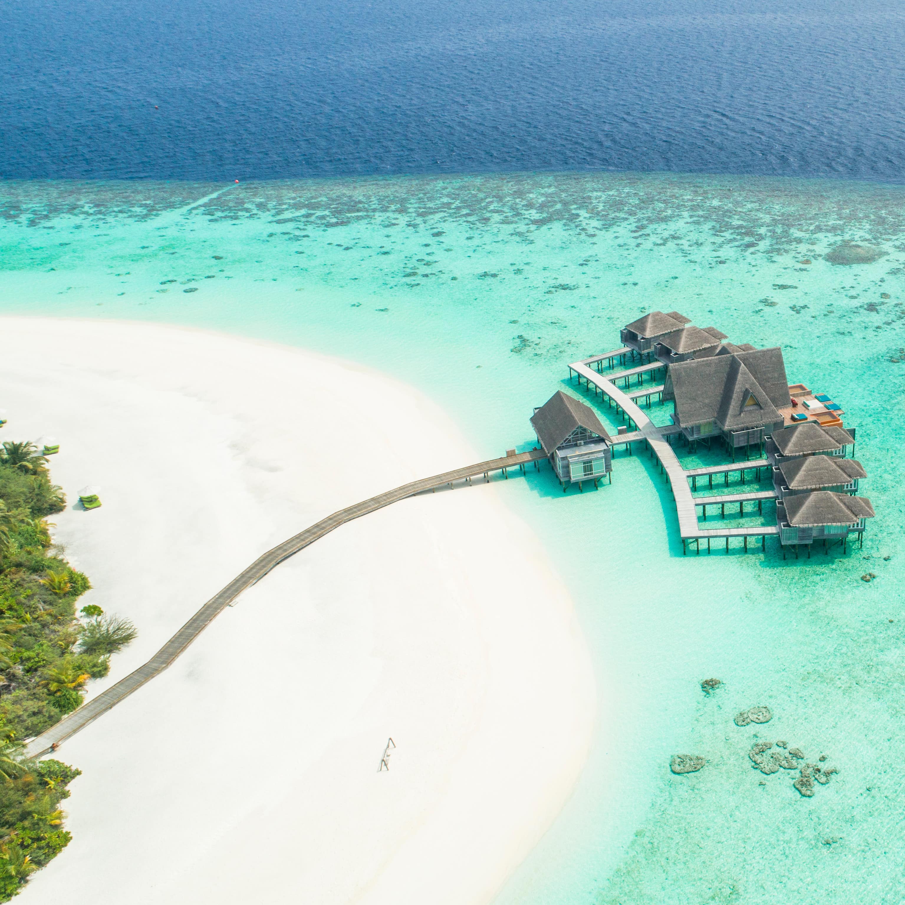 Aerial view of the floating villas on the Kihavah Huravalhi Baa Atoll with aquamarine water and visible reefs