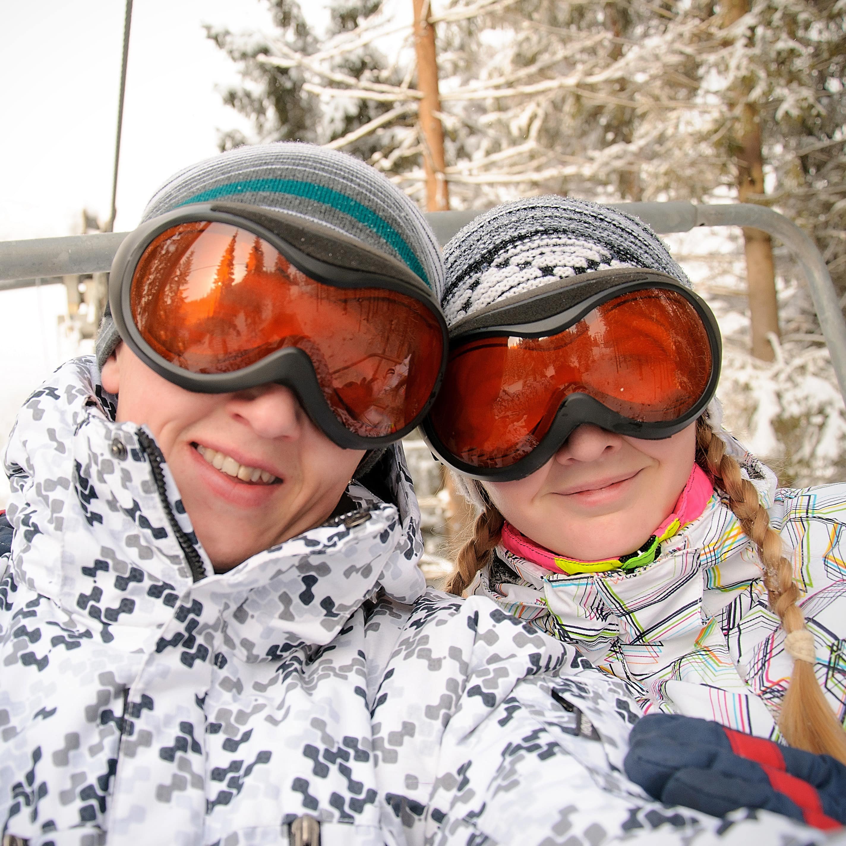 Two smiling ladies on ski lift with red and black goggles