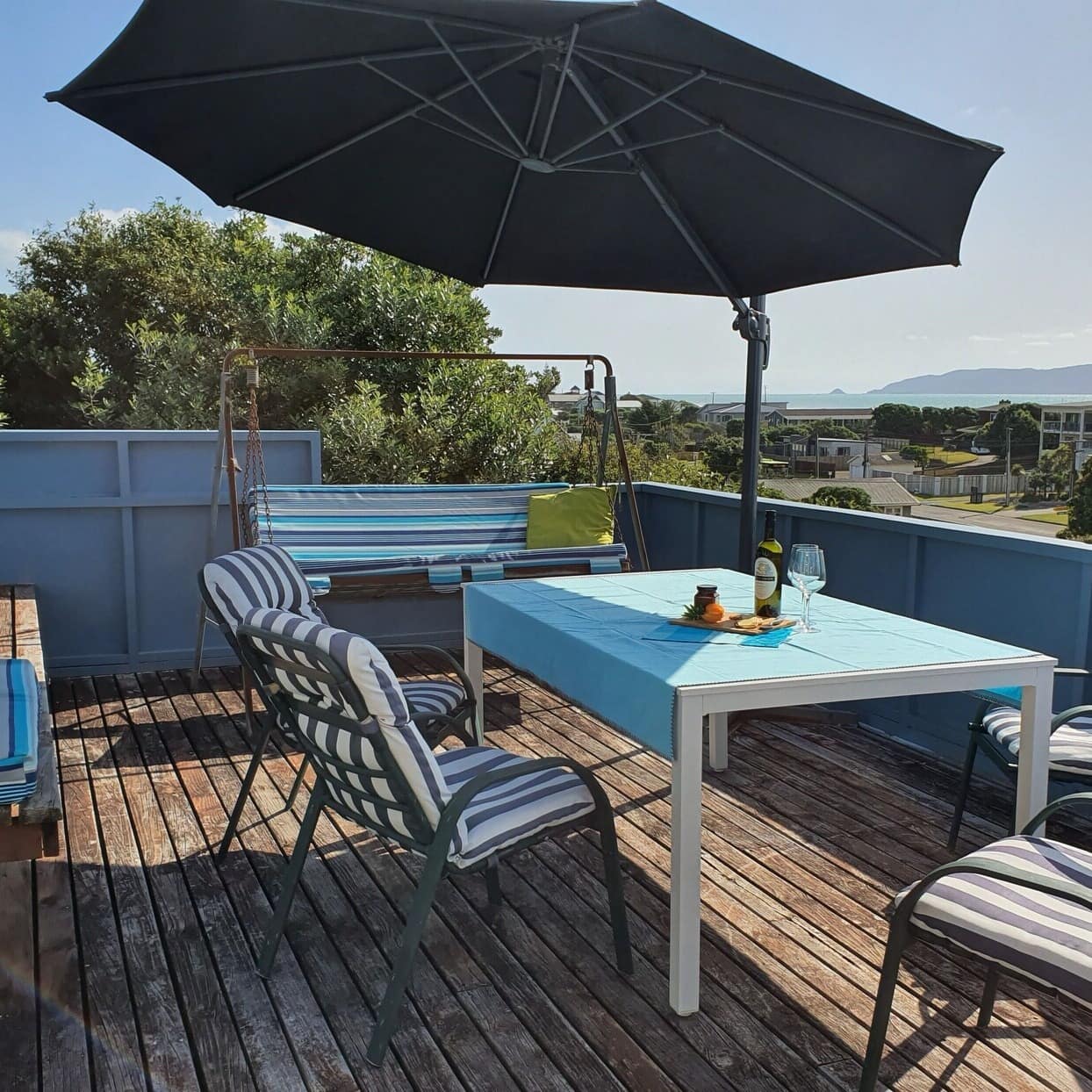 Back deck of a holiday home with a table under an umbrella overlooking the neighbourhood and beach in the distance
