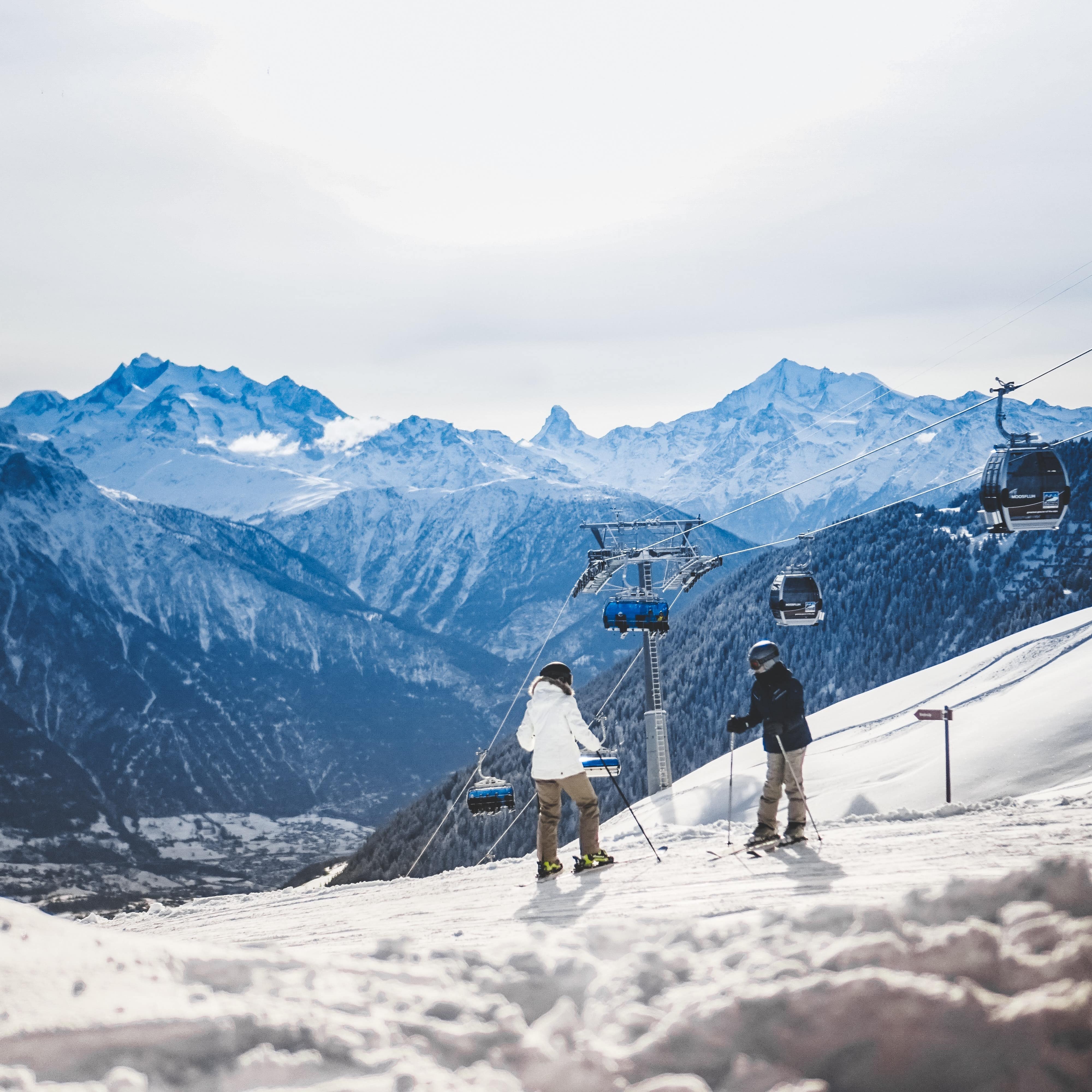 Two skiers at the top of Mount Ruapehu with a chairlift and a view of the mountain range in the distance