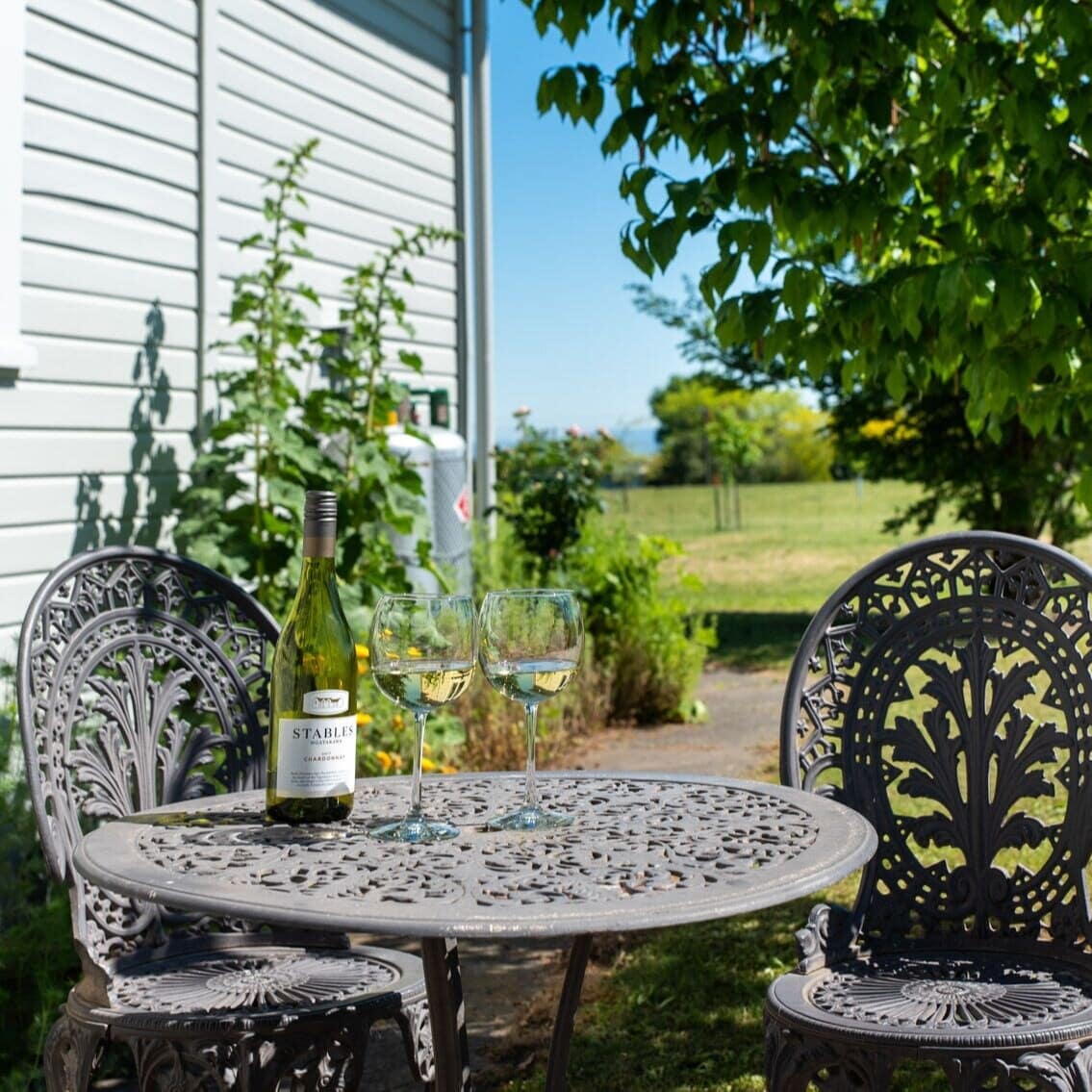 Two garden chairs with a wine bottle and two glasses beside a house on a bright sunny day