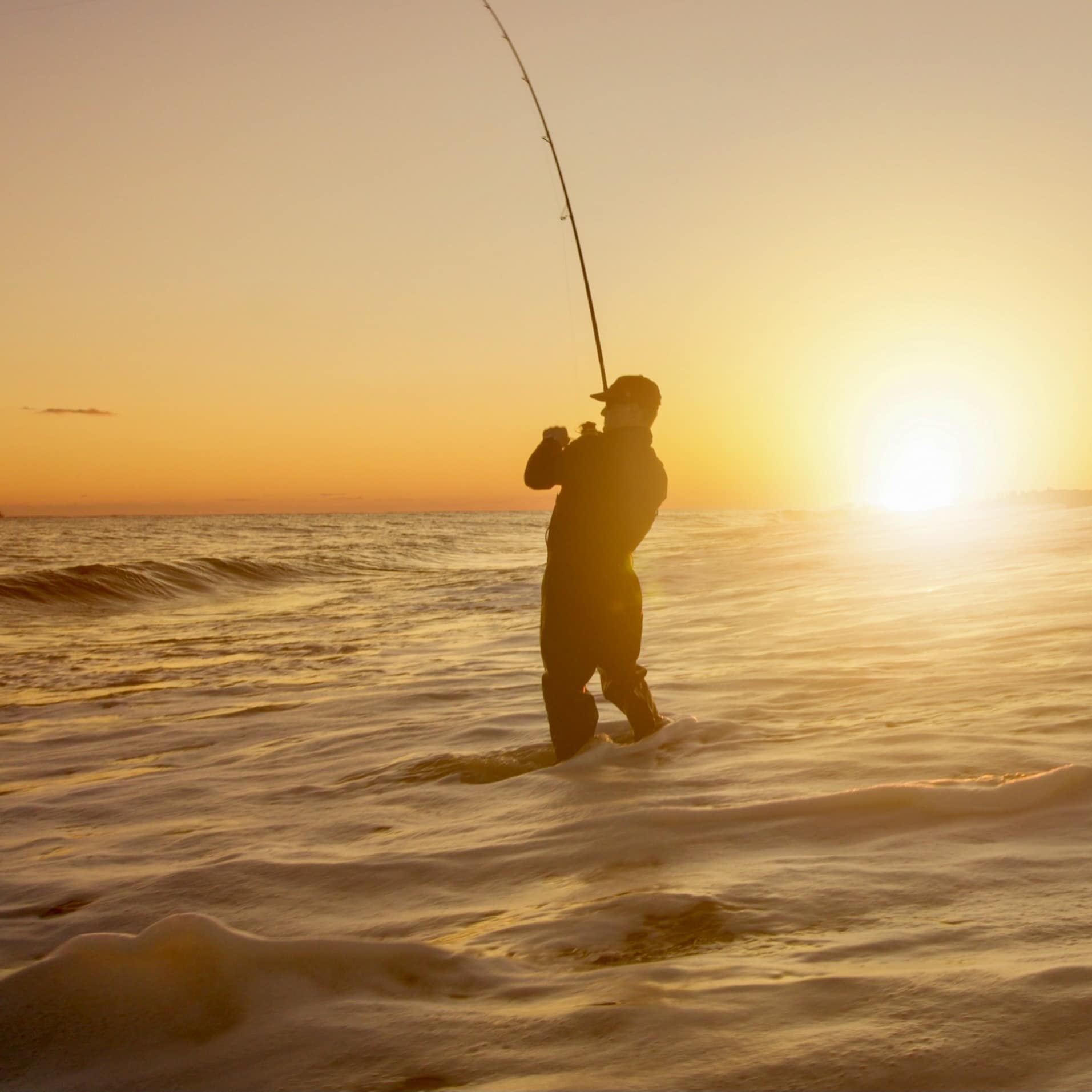Silhouette of a man standing in the ocean water fishing at sunset