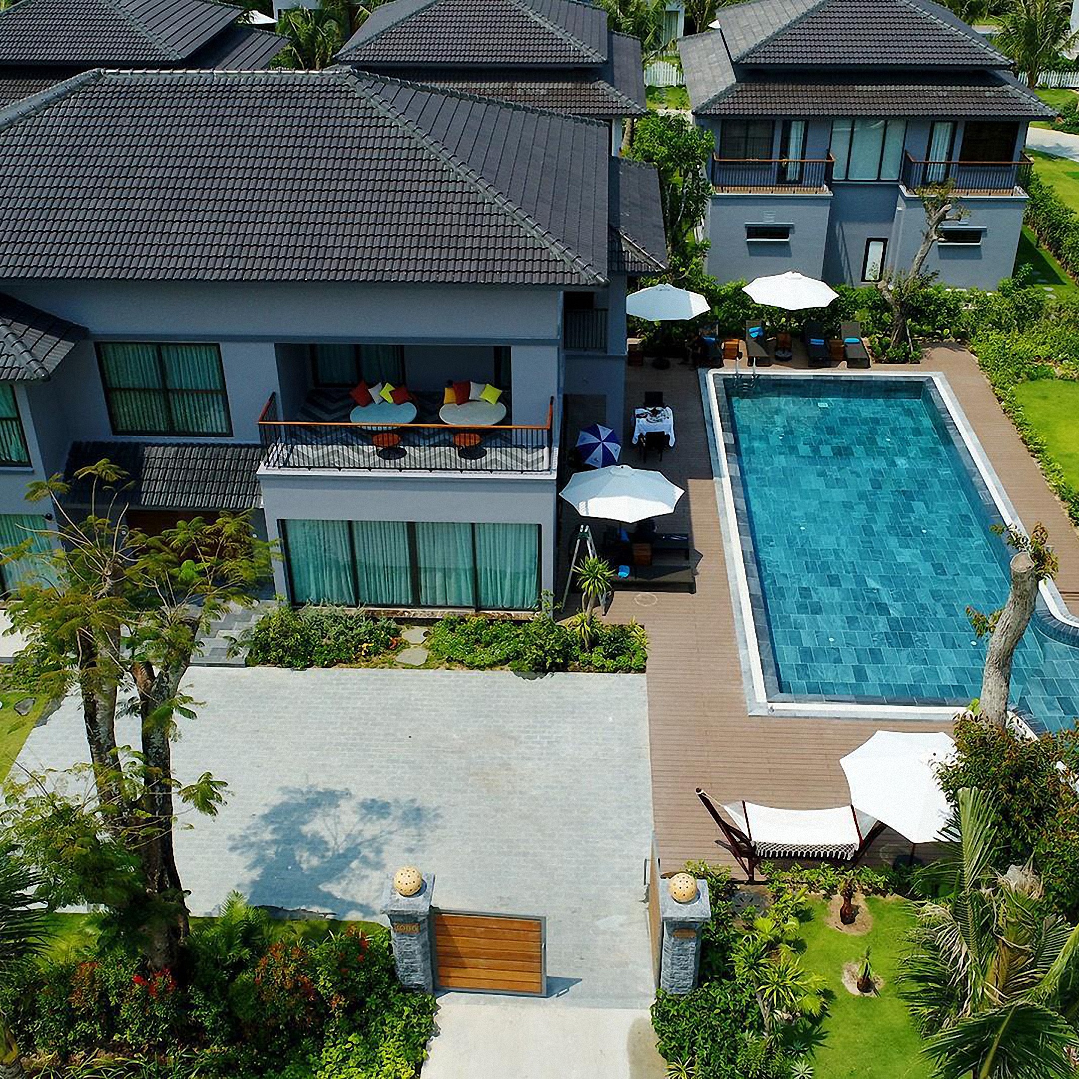 2-storey villa in garden with many windows and a 2nd-floor balcony with tables and a pool with tropical plants