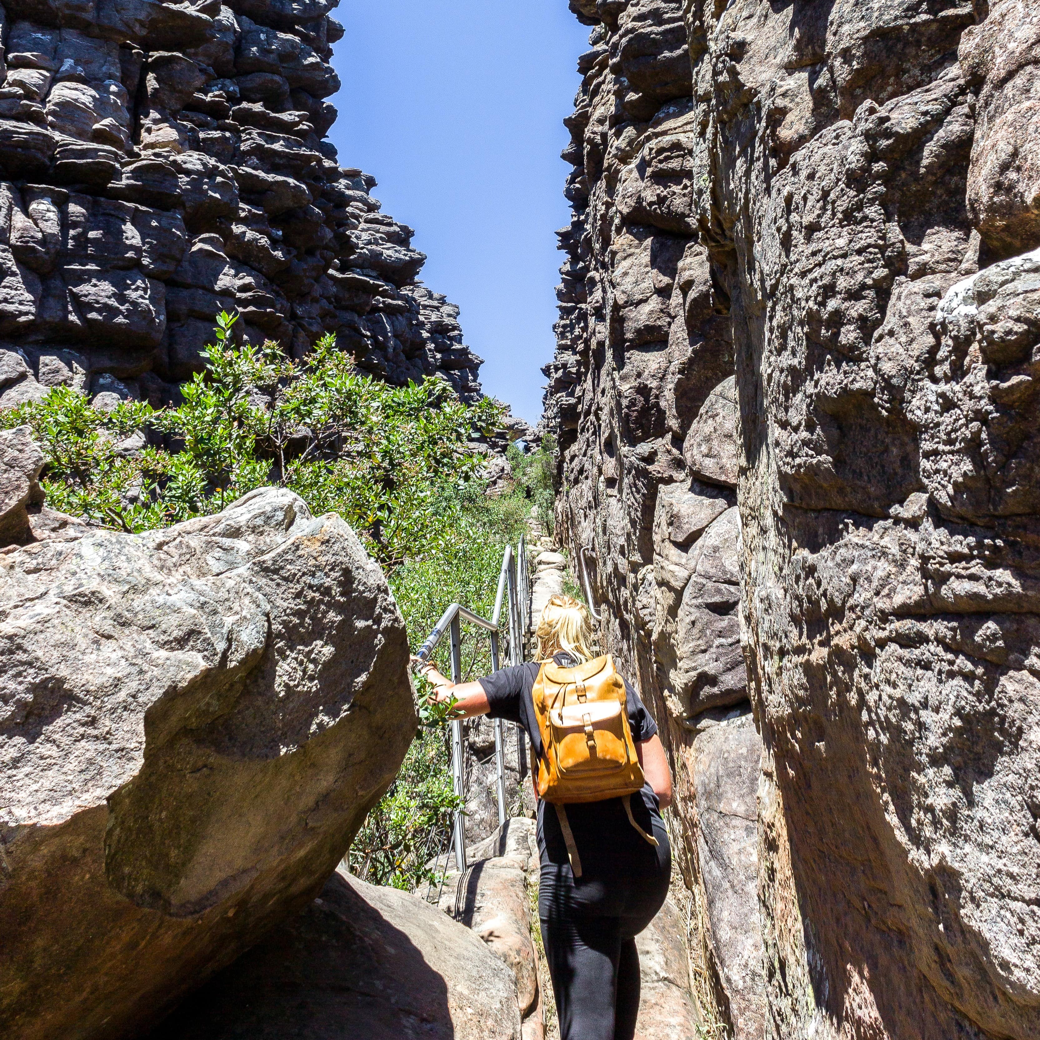 Young woman with backpack on holding rail as she hikes to the pinnacle lookout, The Central Grampians, Victoria, Australia
