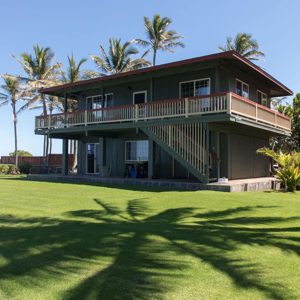 A Polynesian house with a mowed lawn and palm trees in its yard