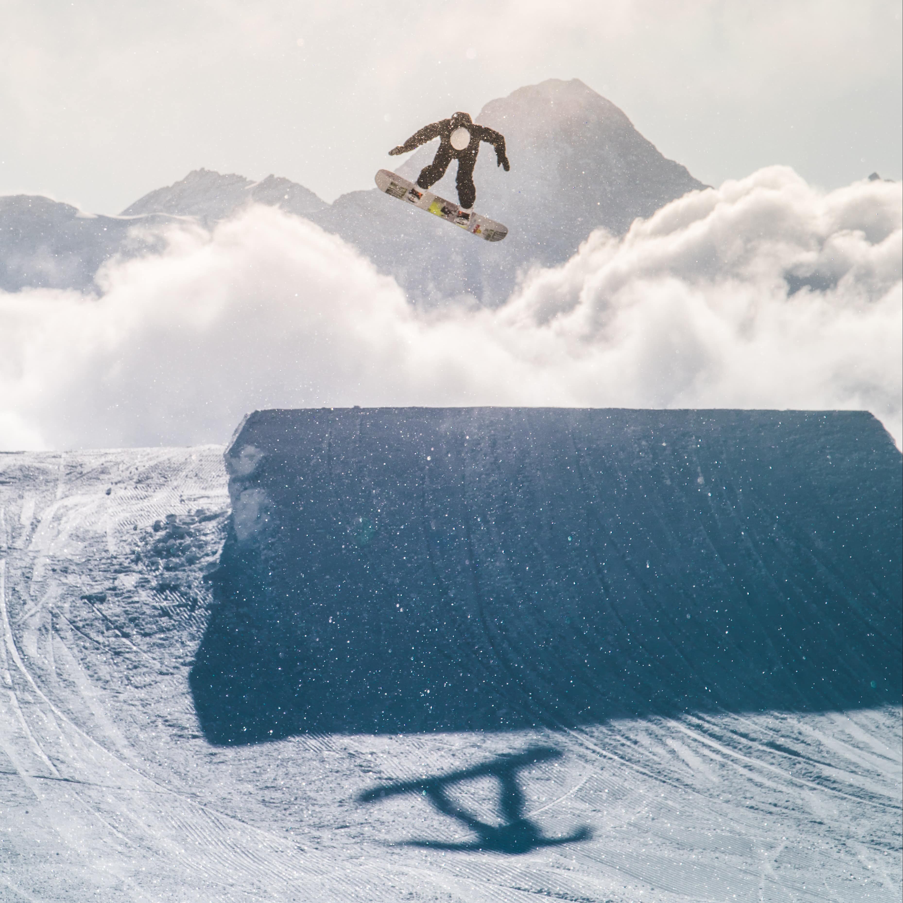 Snowboarder in black snowsuit doing jump on snow covered ramp