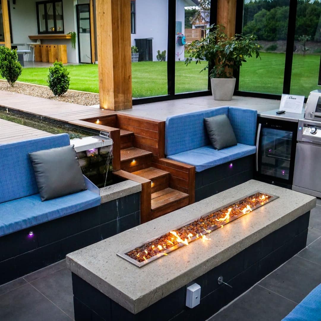 An indoor fire pit of a luxury family home surrounded by blue couches and a TV