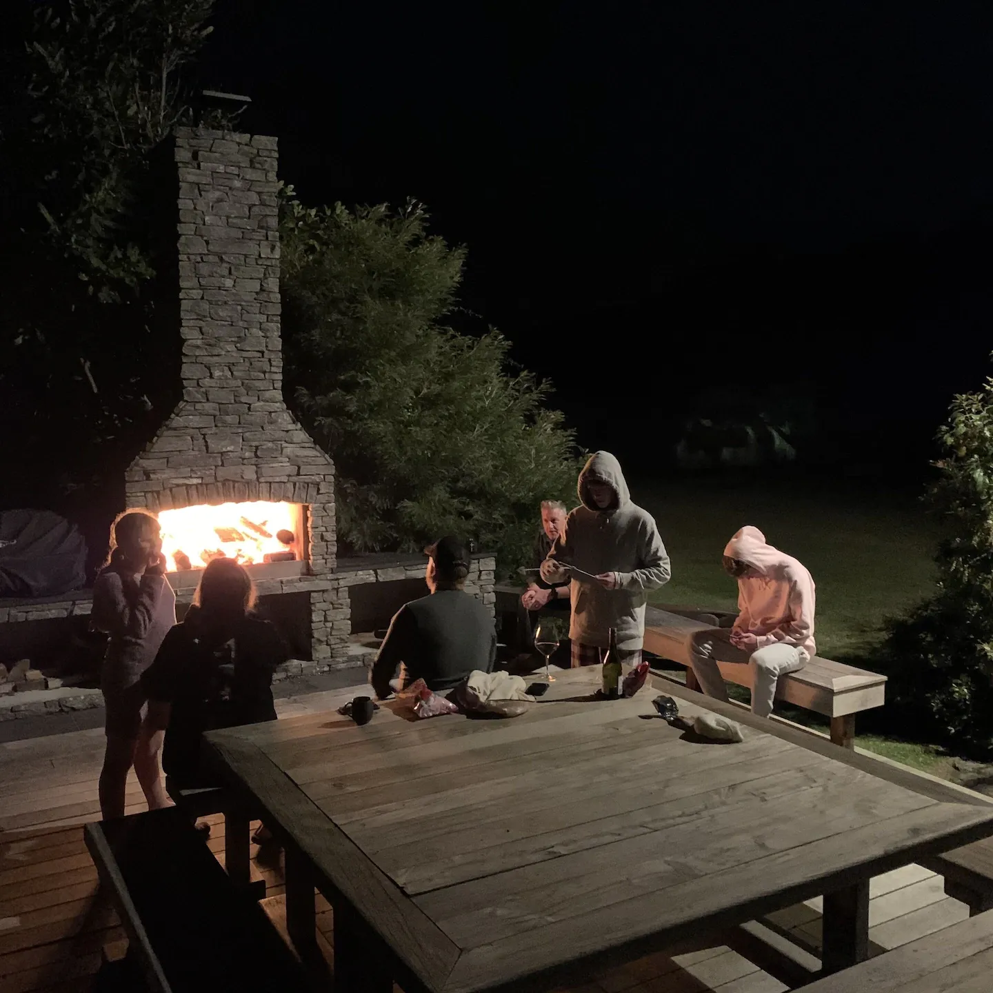 Family sitting outside by the fireplace on private deck at night