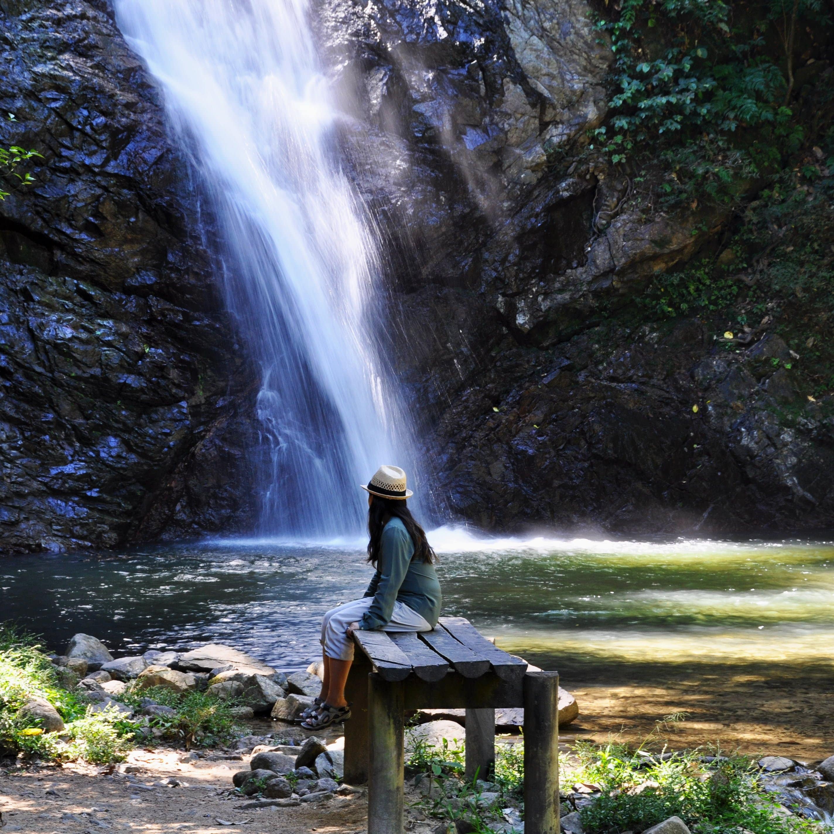 A lady sitting and taking in the scenery while a waterfall cascades down a hillside.