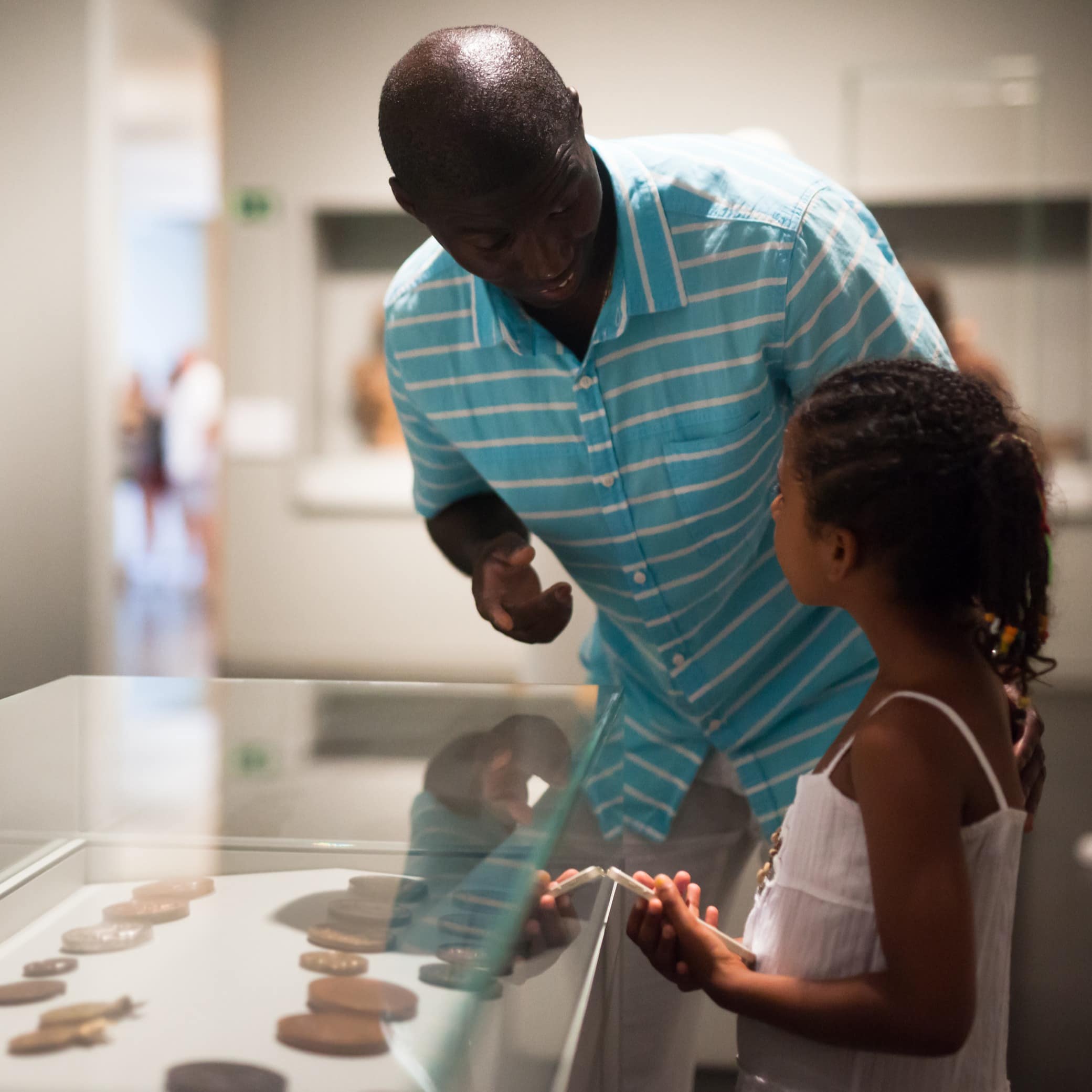 Father and his little daughter visiting museum and looking at showcase with exhibits