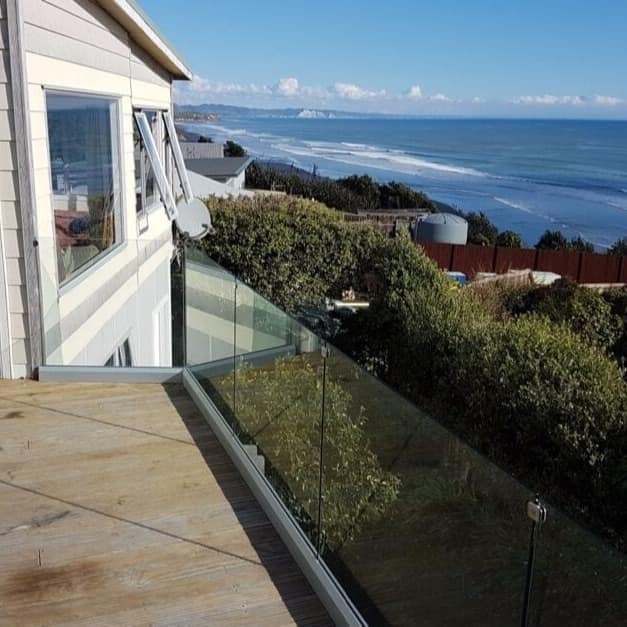 View from the wooden deck of a home overlooking the vegetation and ocean on a bright blue day