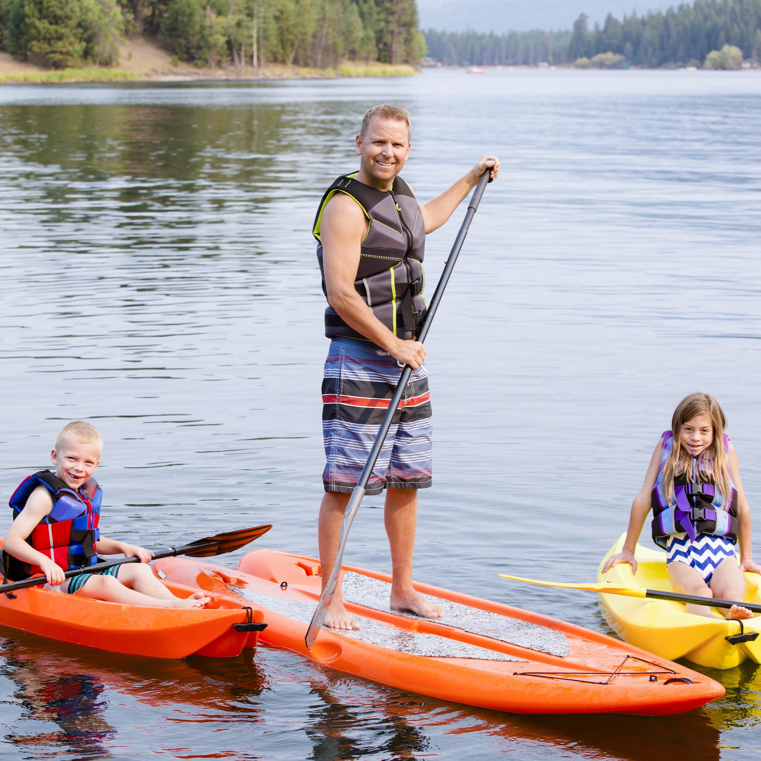 Dad and two kids kayaking and paddleboarding together on lake
