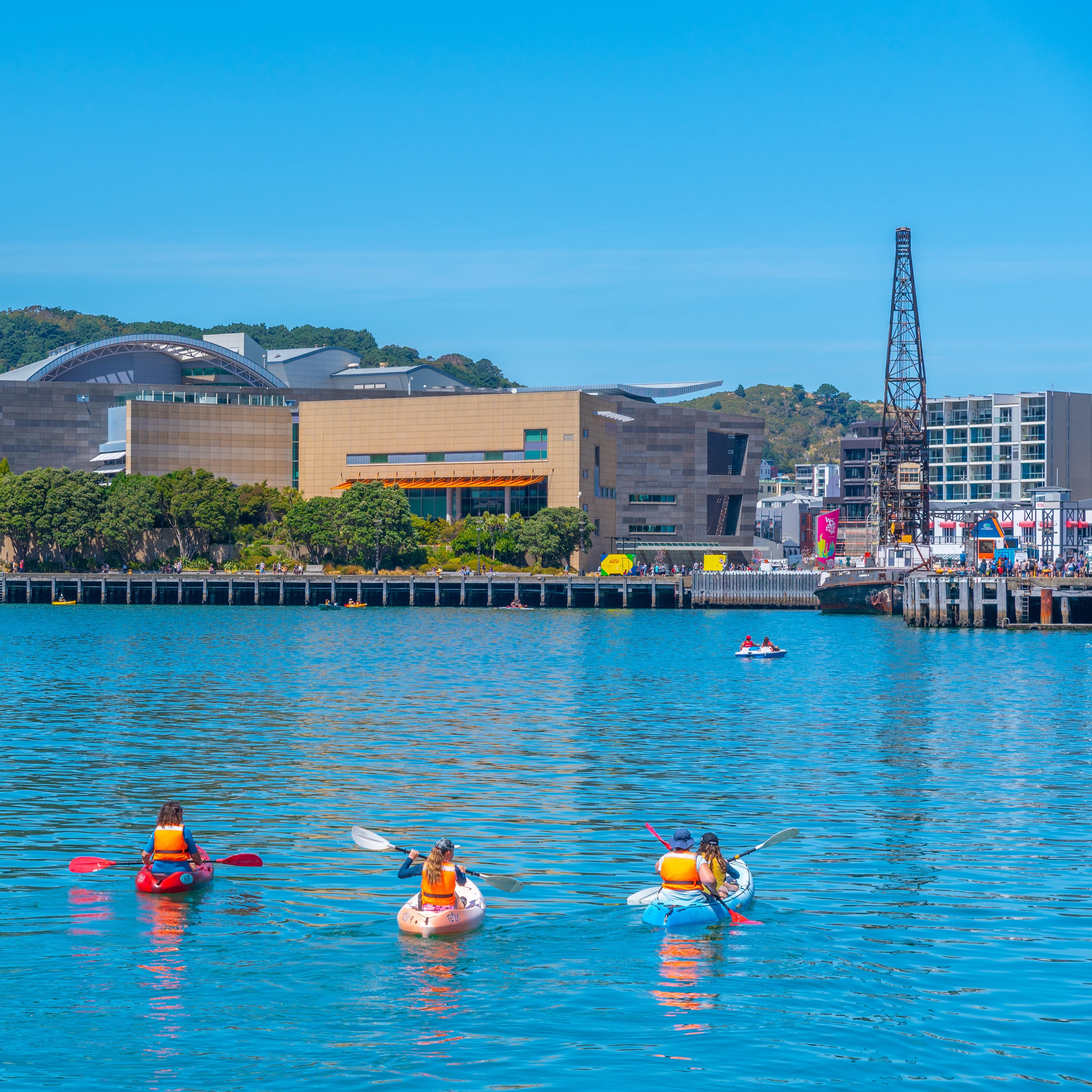 People in kayaks paddle toward Museum of New Zealand Te Papa Tongarewa in Wellington, New Zealand