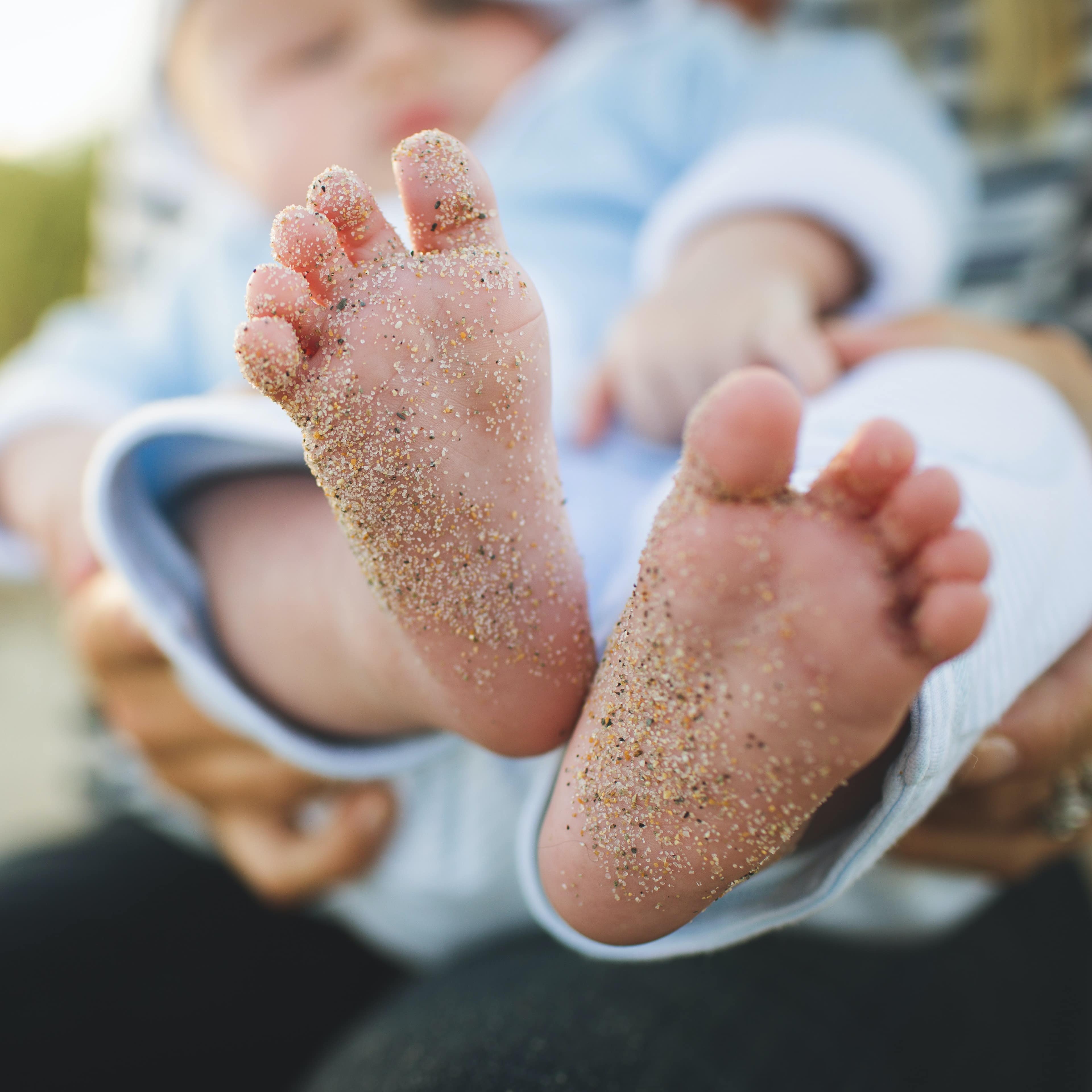 Bottom of baby's sandy feet being held up for the camera