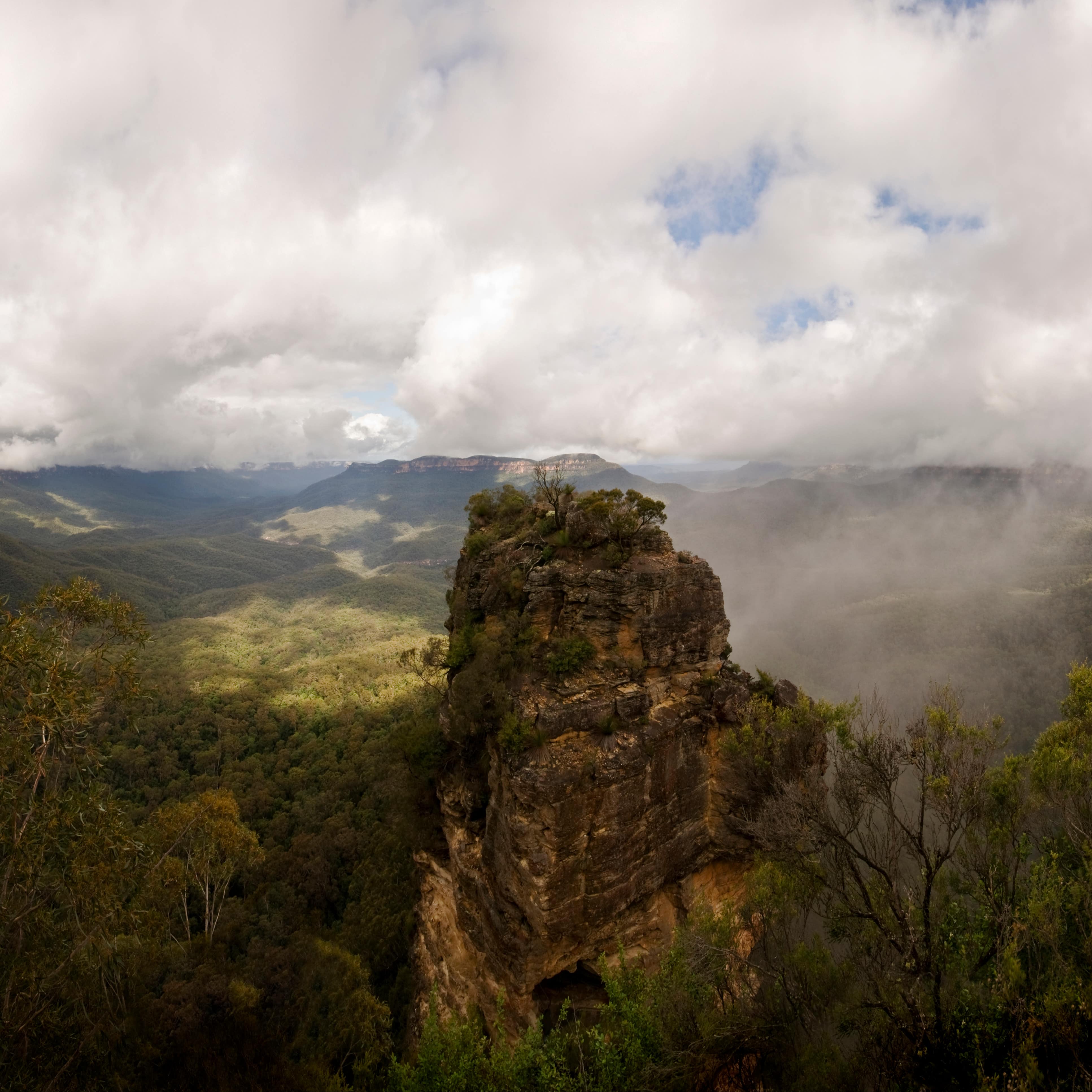 A rock formation in the Blue Mountains region surrounded by forests and mountains in the clouds