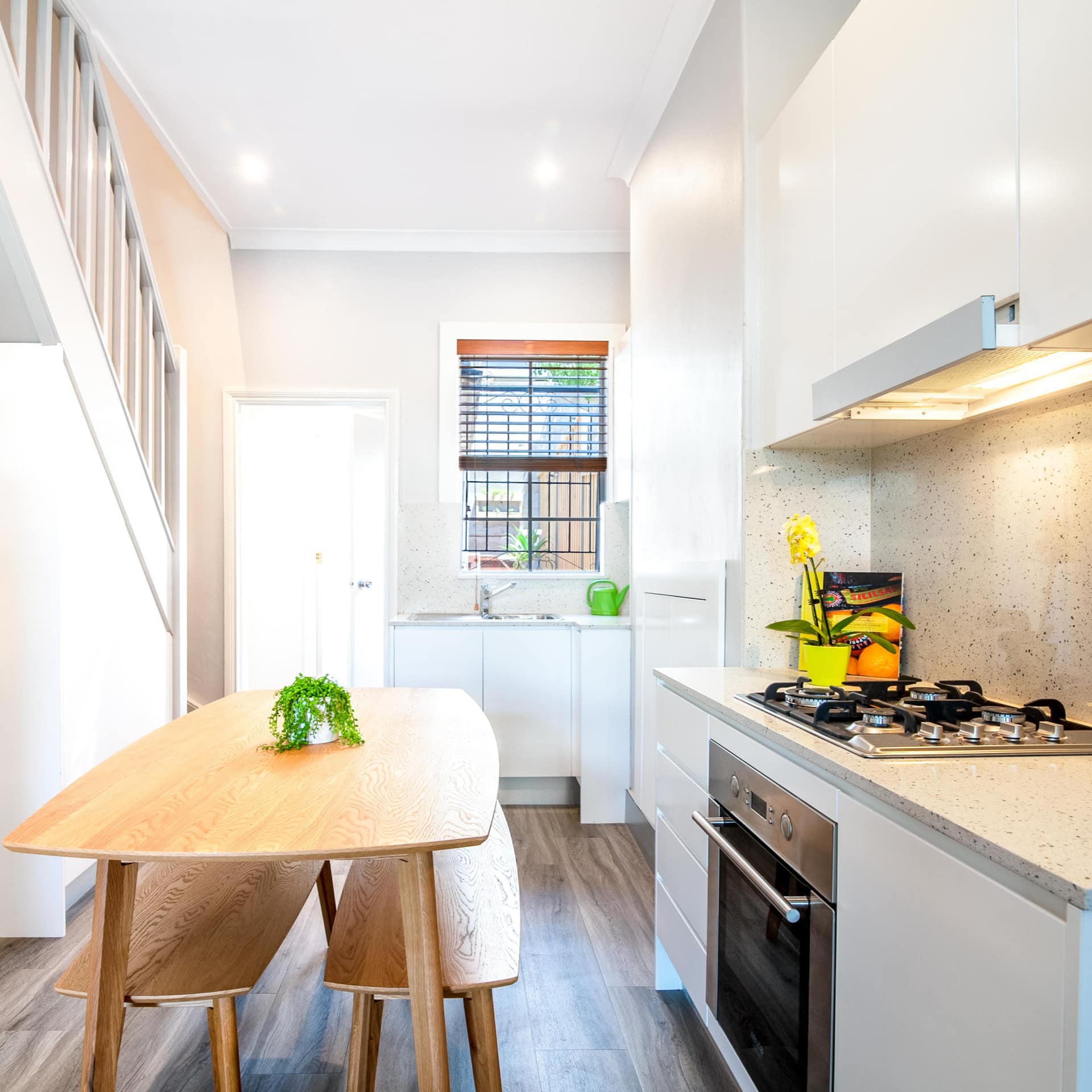 Modern kitchen and dining room with hardwood floors, white walls, wood dining table and benches, and white cabinets.
