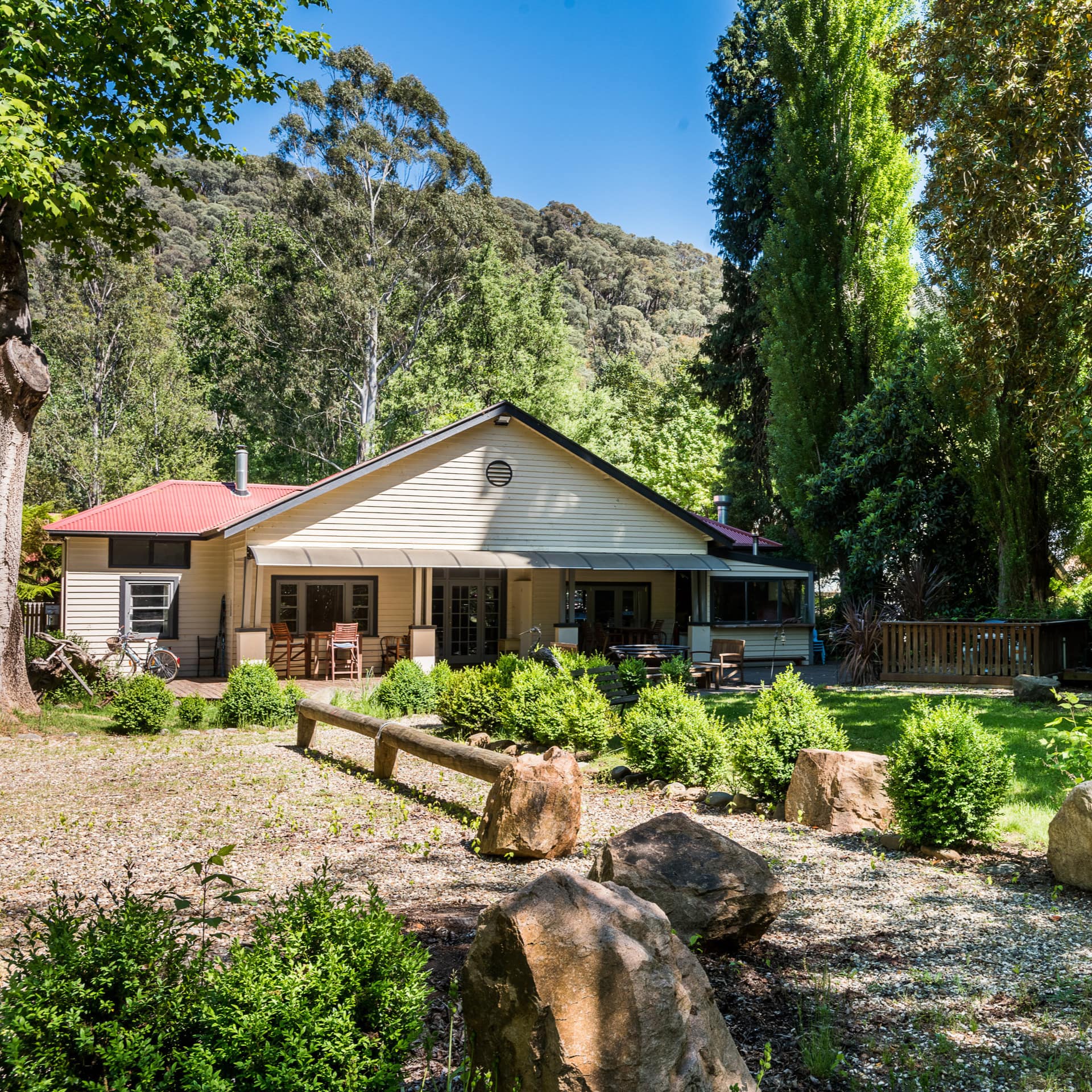 View of a white cottage with red roof, landscaped lawn, gravel pathway and driveway, surrounded by rural landscape.