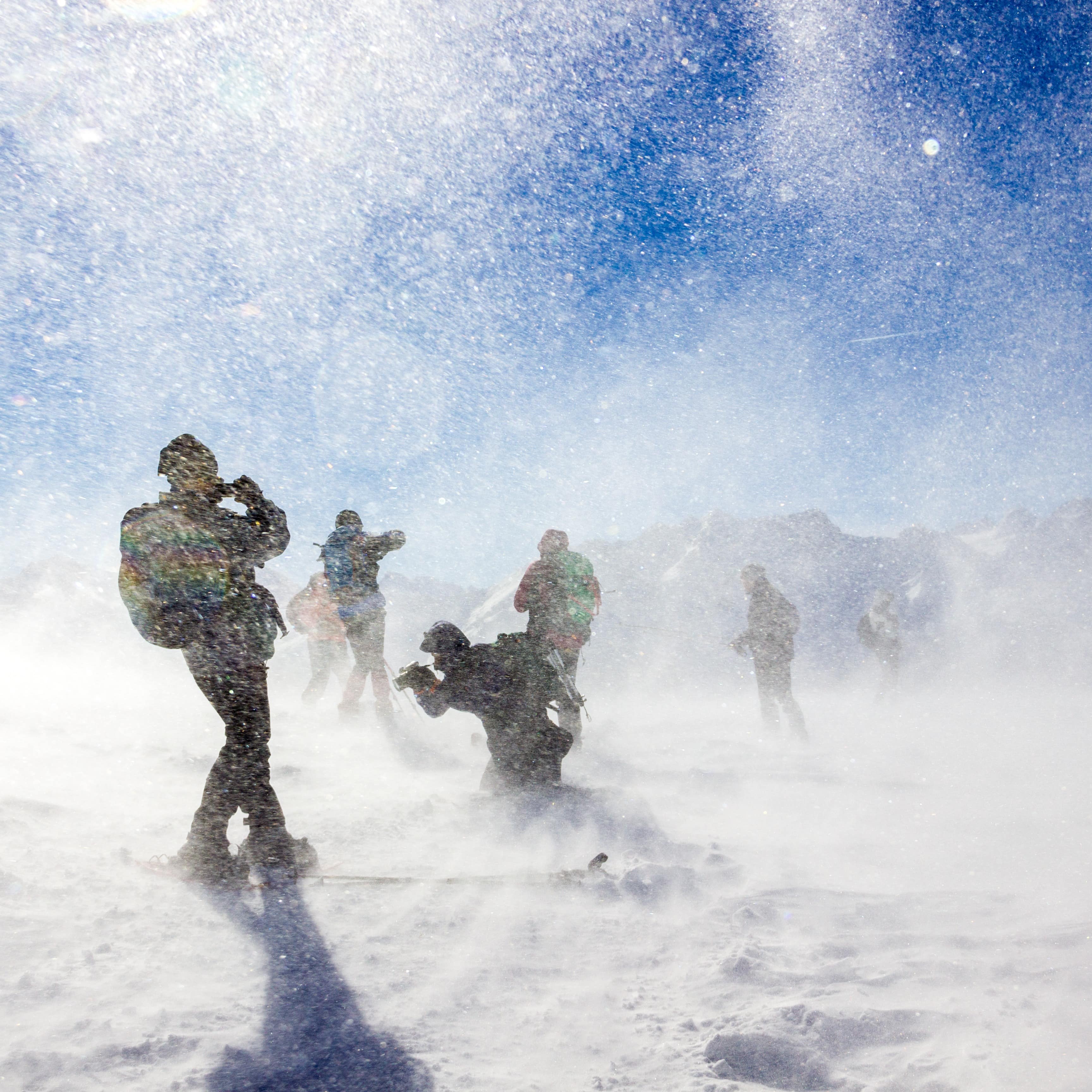 People exploring in a snowstorm with blue sky ice mountains in the background