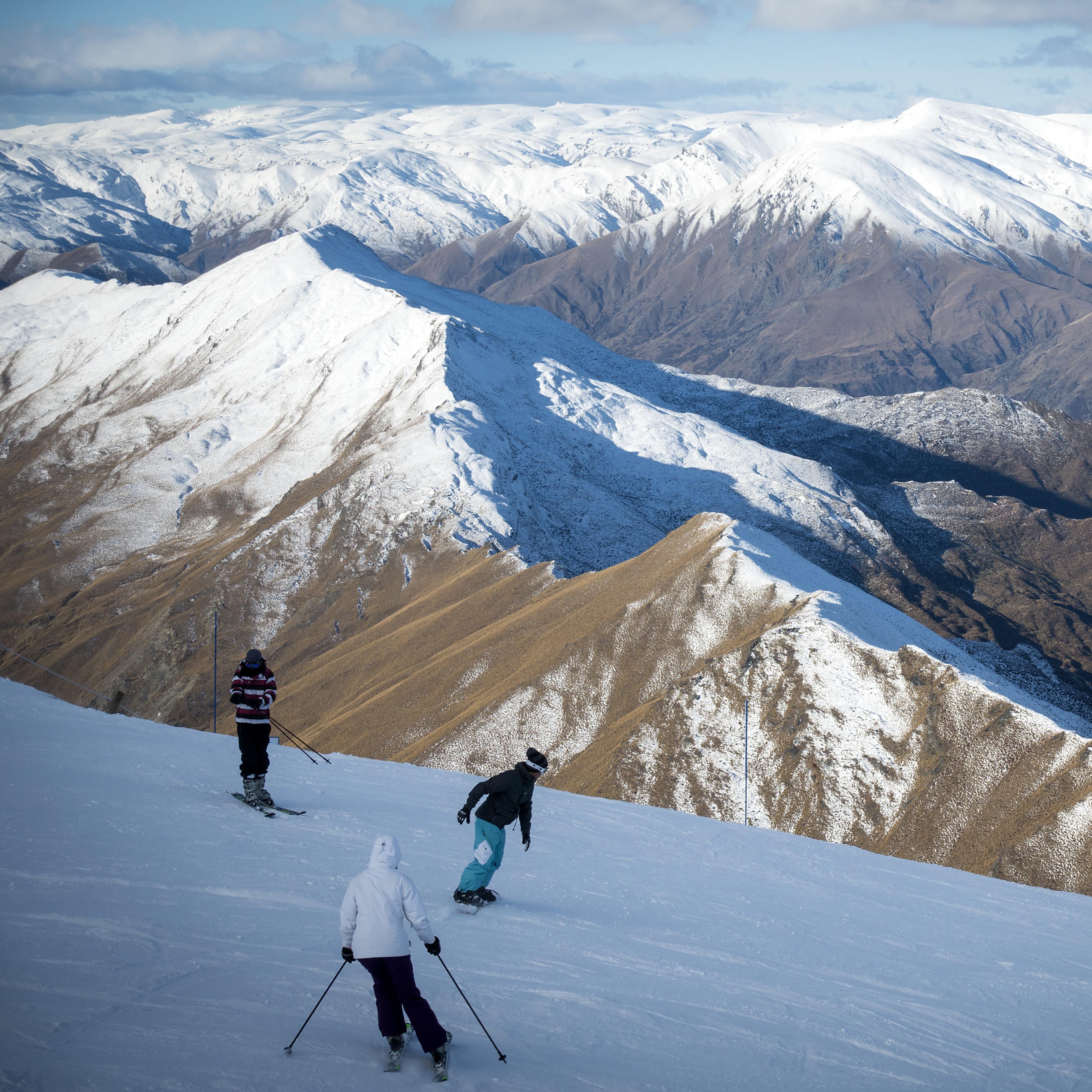 Some skiers coming down the slopes with snow covered mountains surrounding them.