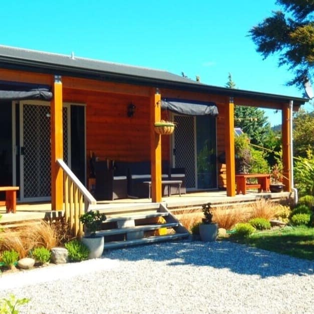 A small lakefront cottage surrounded by trees and bushes under a bright blue sky