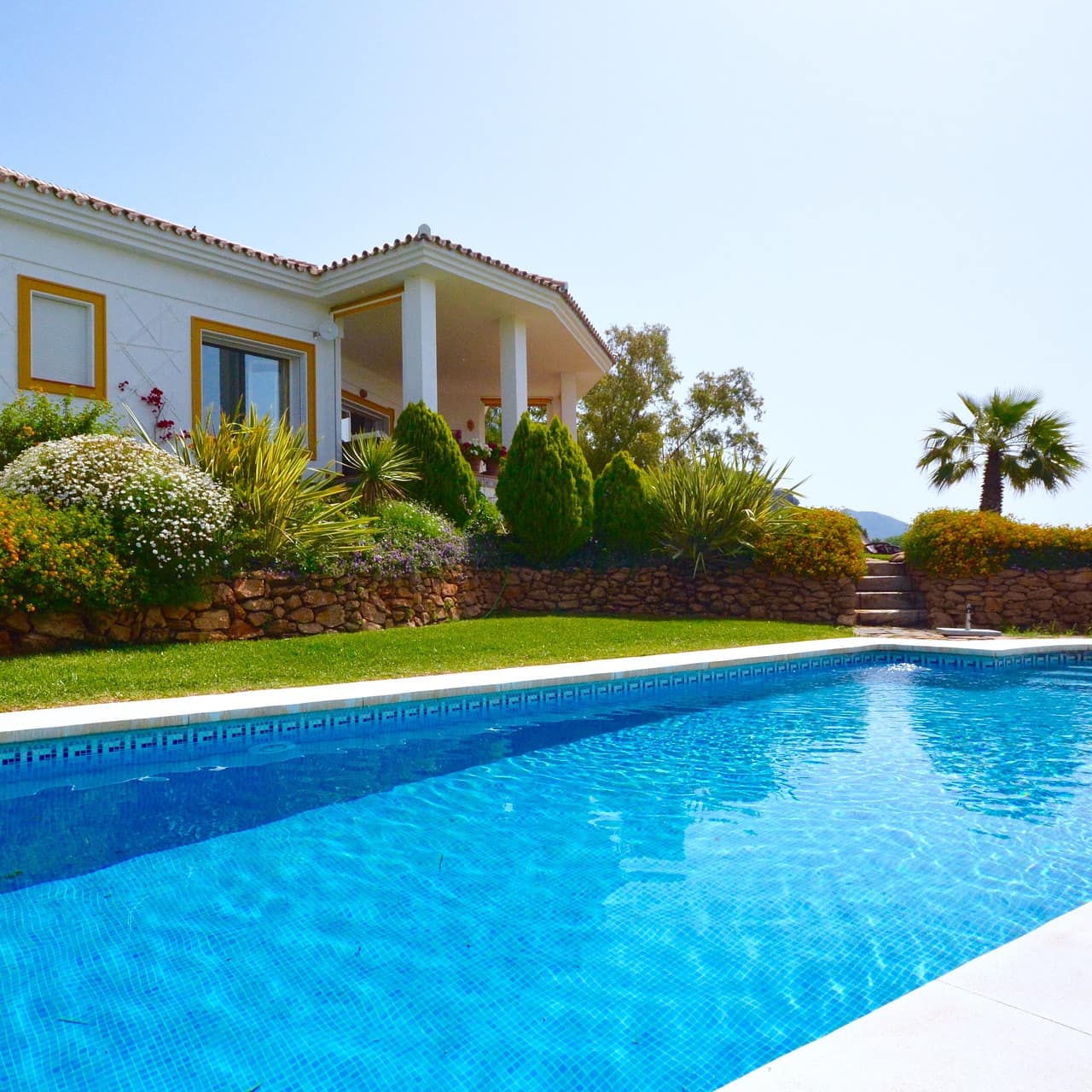 White Spanish villa with a red tile roof, ochre windows and a veranda overlooking a formal garden and rectangular pool