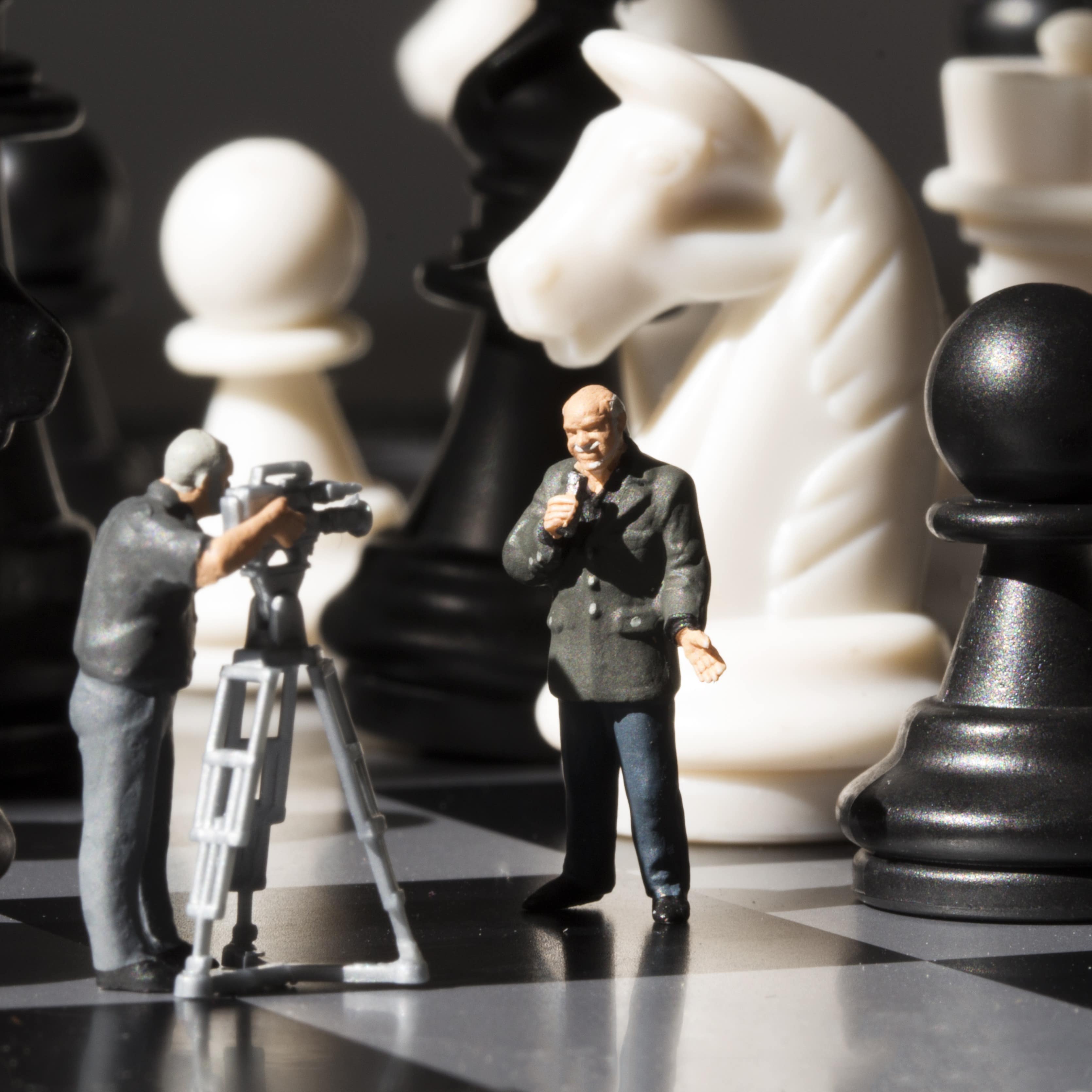 Shows filming chess game process with miniature journalists on a chessboard