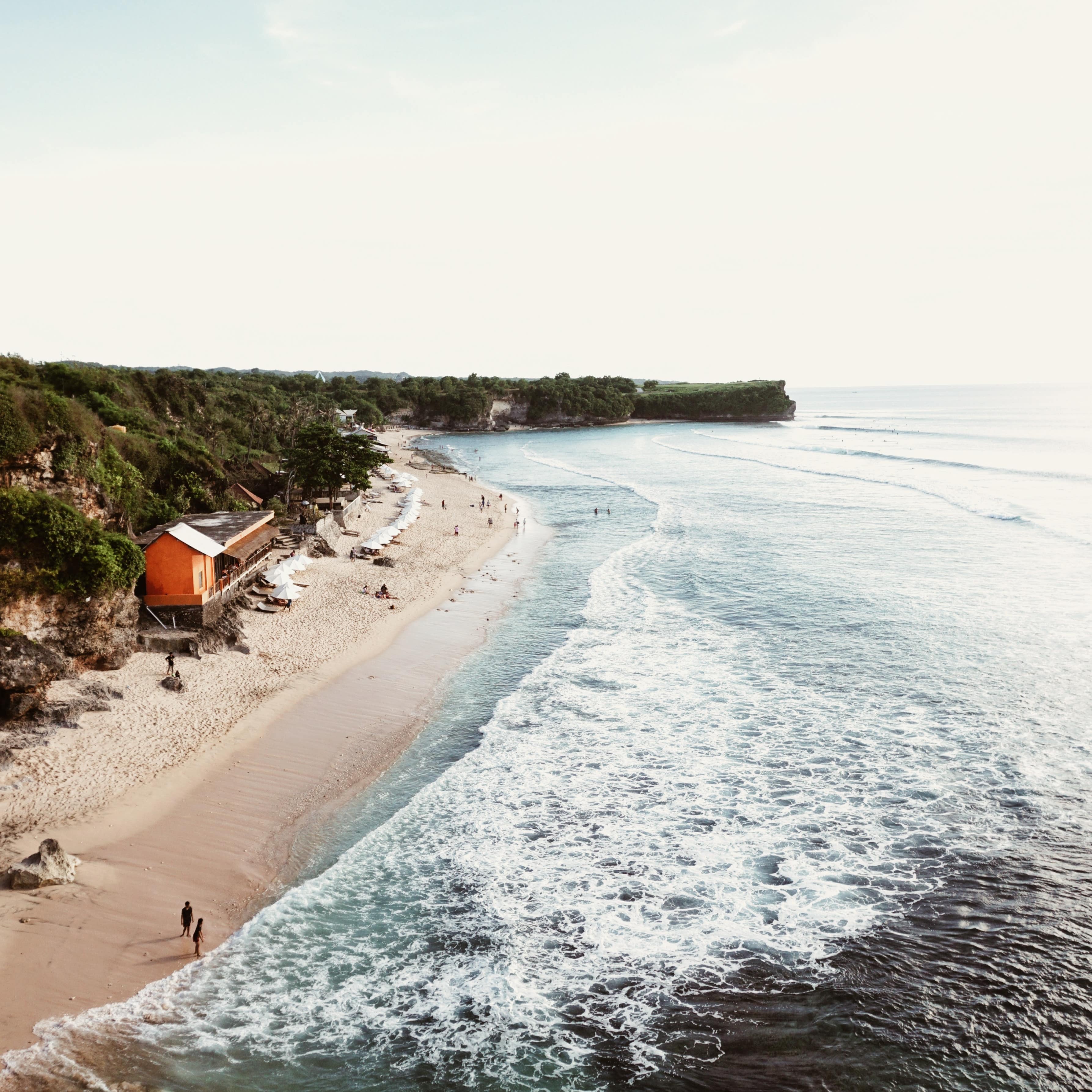 Aerial view of Kuta beach with beachfront villa, pink sands and people enjoying the surf