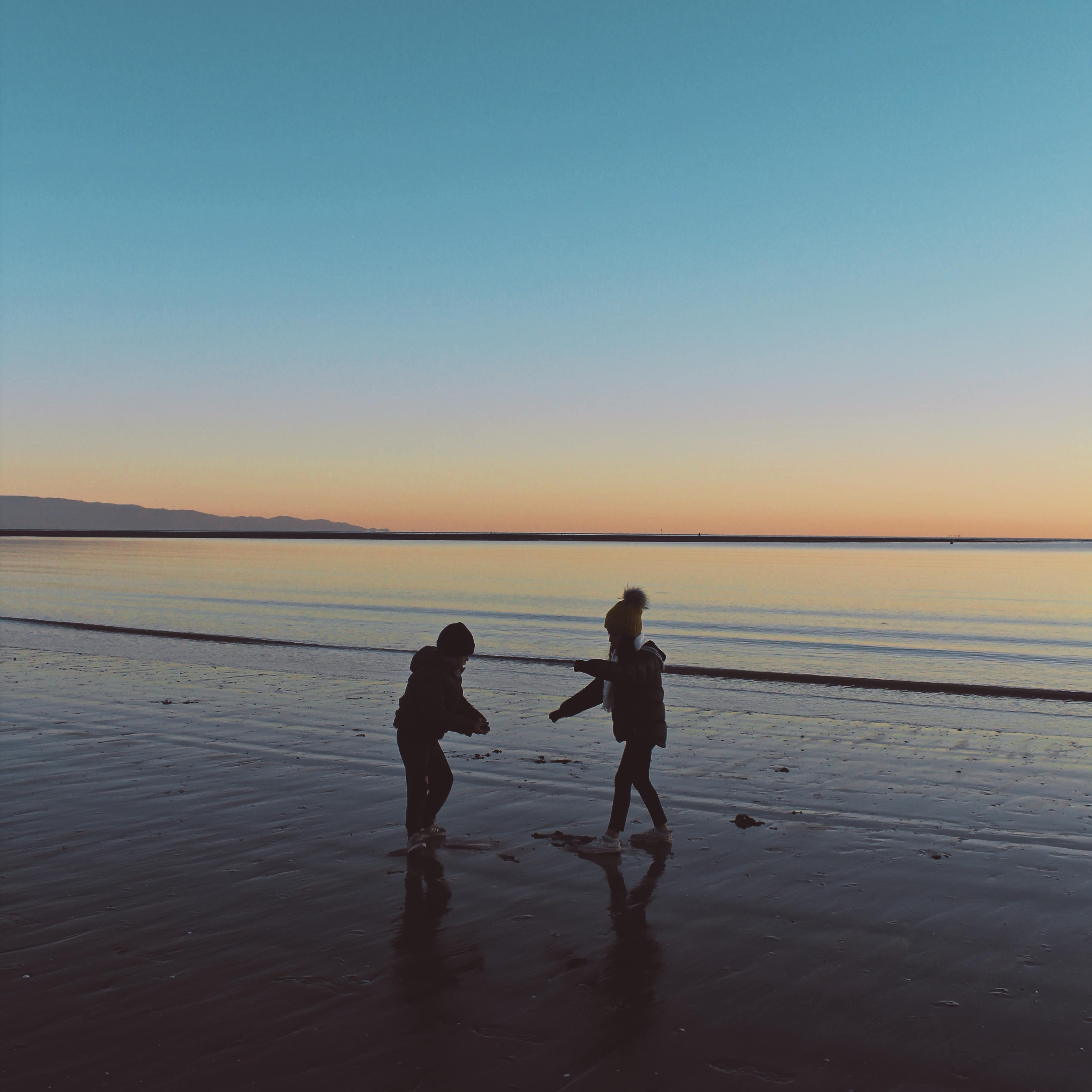 Two children playing on a beach in New Zealand at dusk