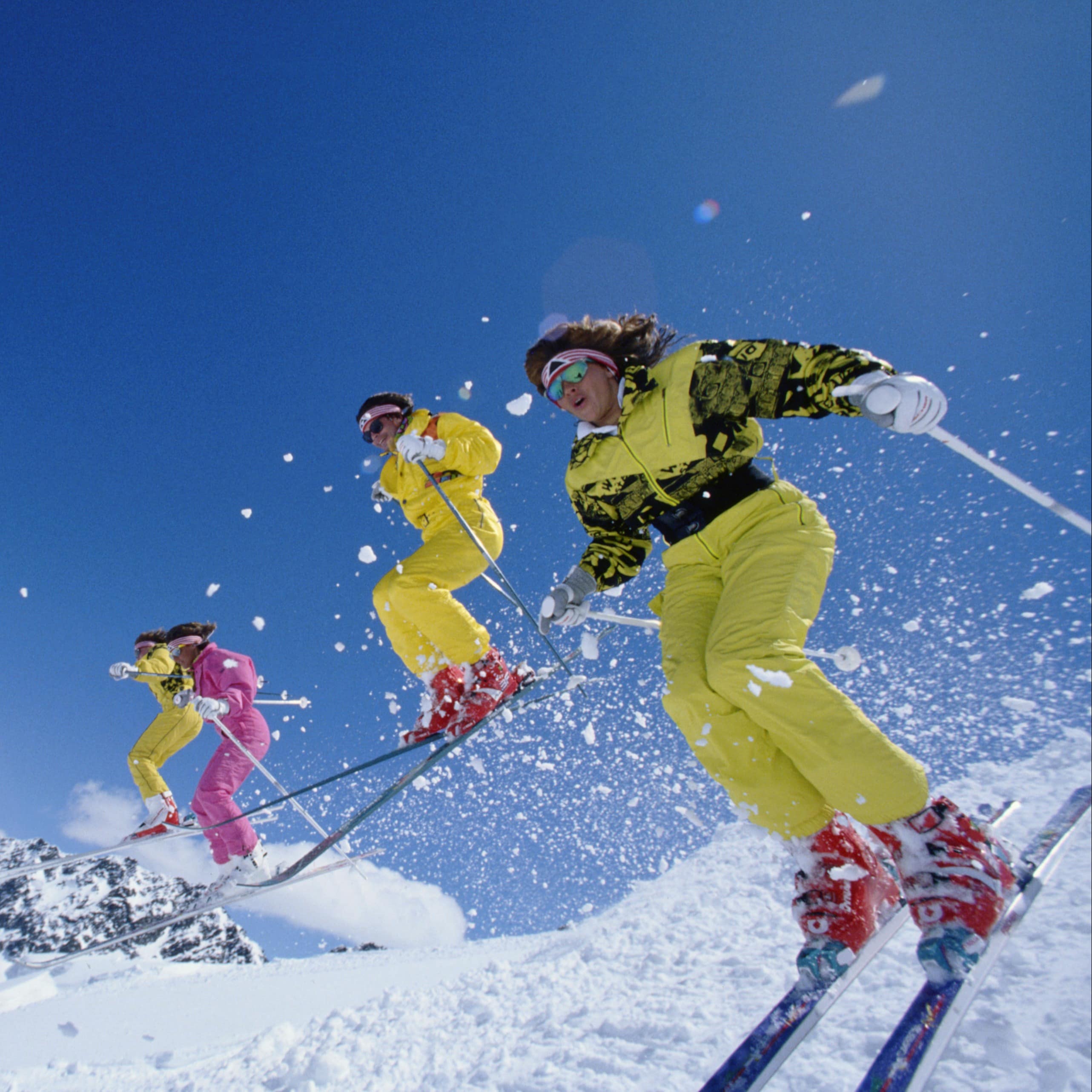 Four skiers headed down slopes, some flying through the air.