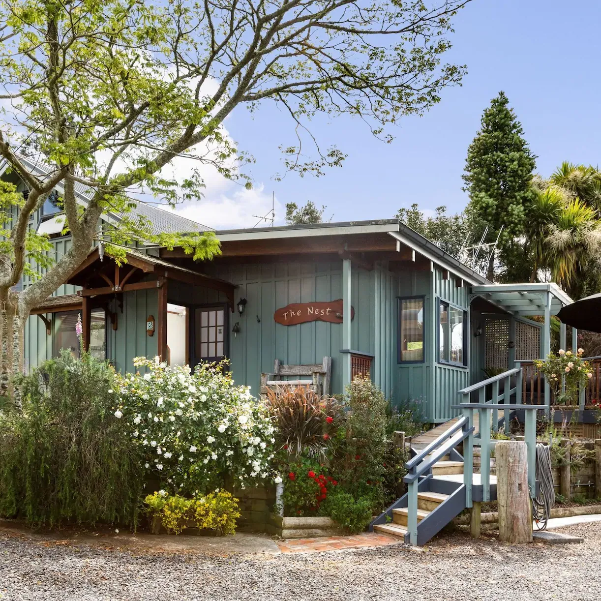 Teal-blue cottage surrounded by trees and flowers