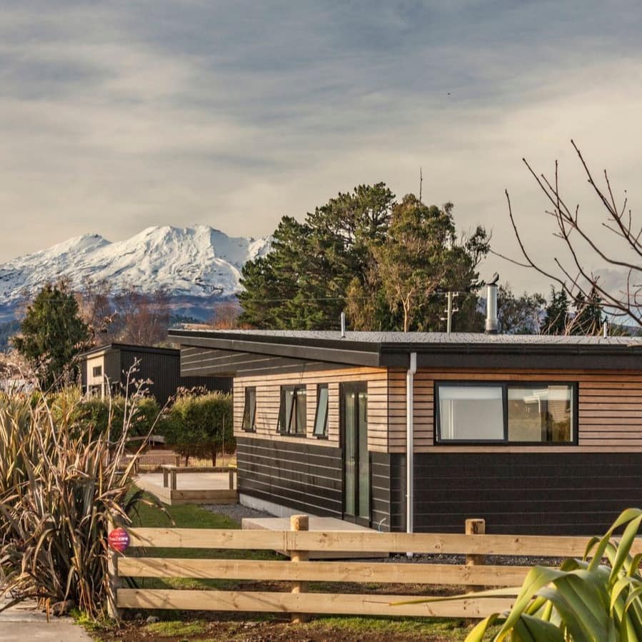 A small, modern mountain home with snow-capped mountains in the background