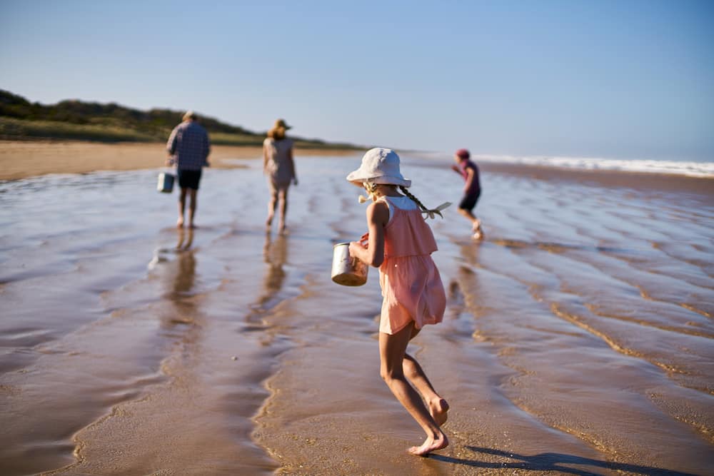 A girl is holding a bucket and running along on a beach towards her family in the Fleurieu Peninsula