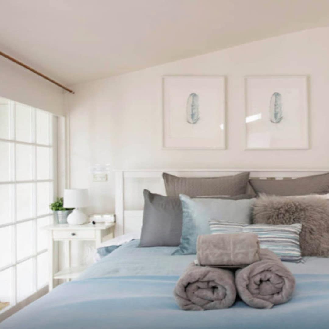 Bedroom space of studio, white walls, queen size bed, blue and grey bedding, and french glass doors to the courtyard.