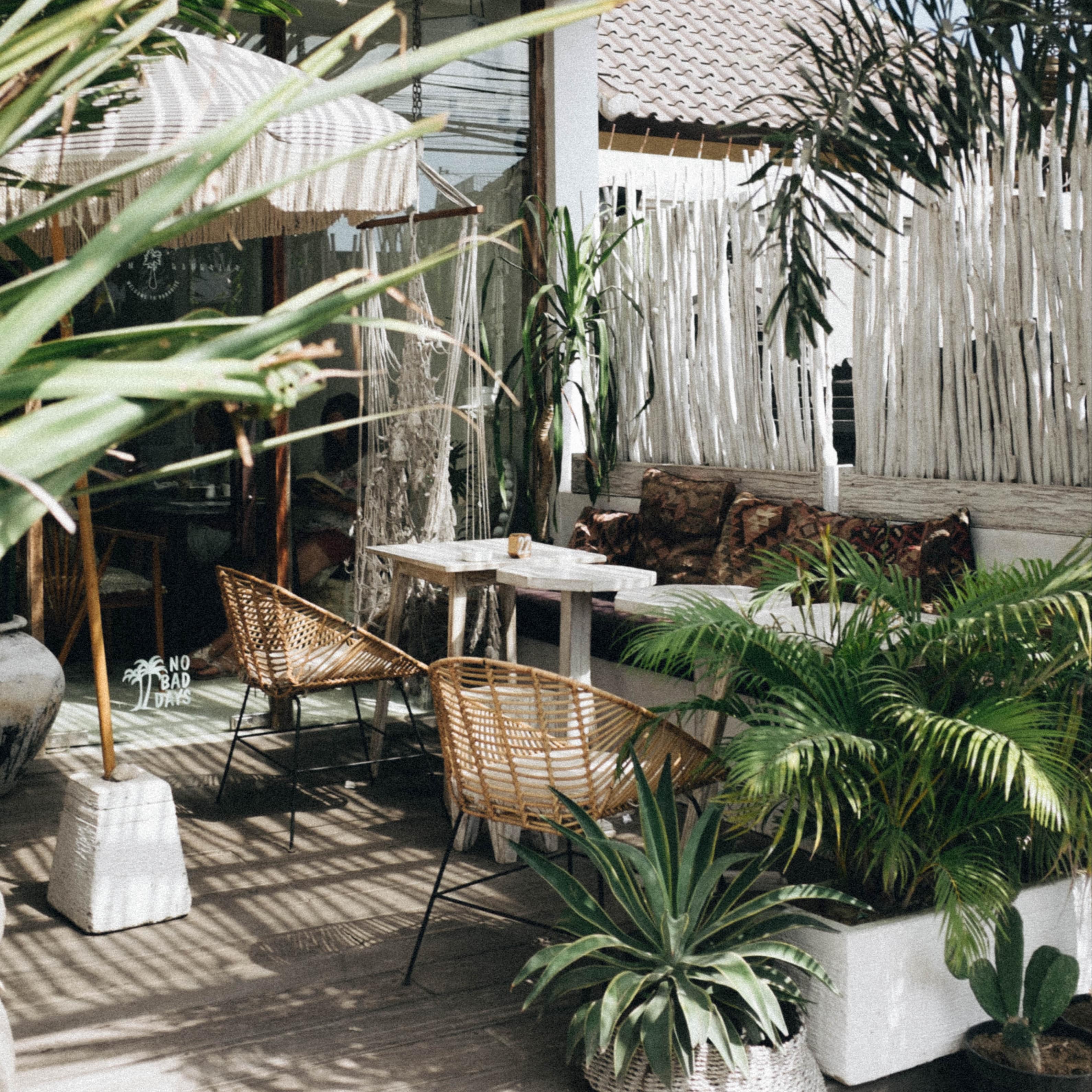 Deck of villa with an outdoor bench seat, wicker chairs, potted plants and a shade umbrella with a white arbour