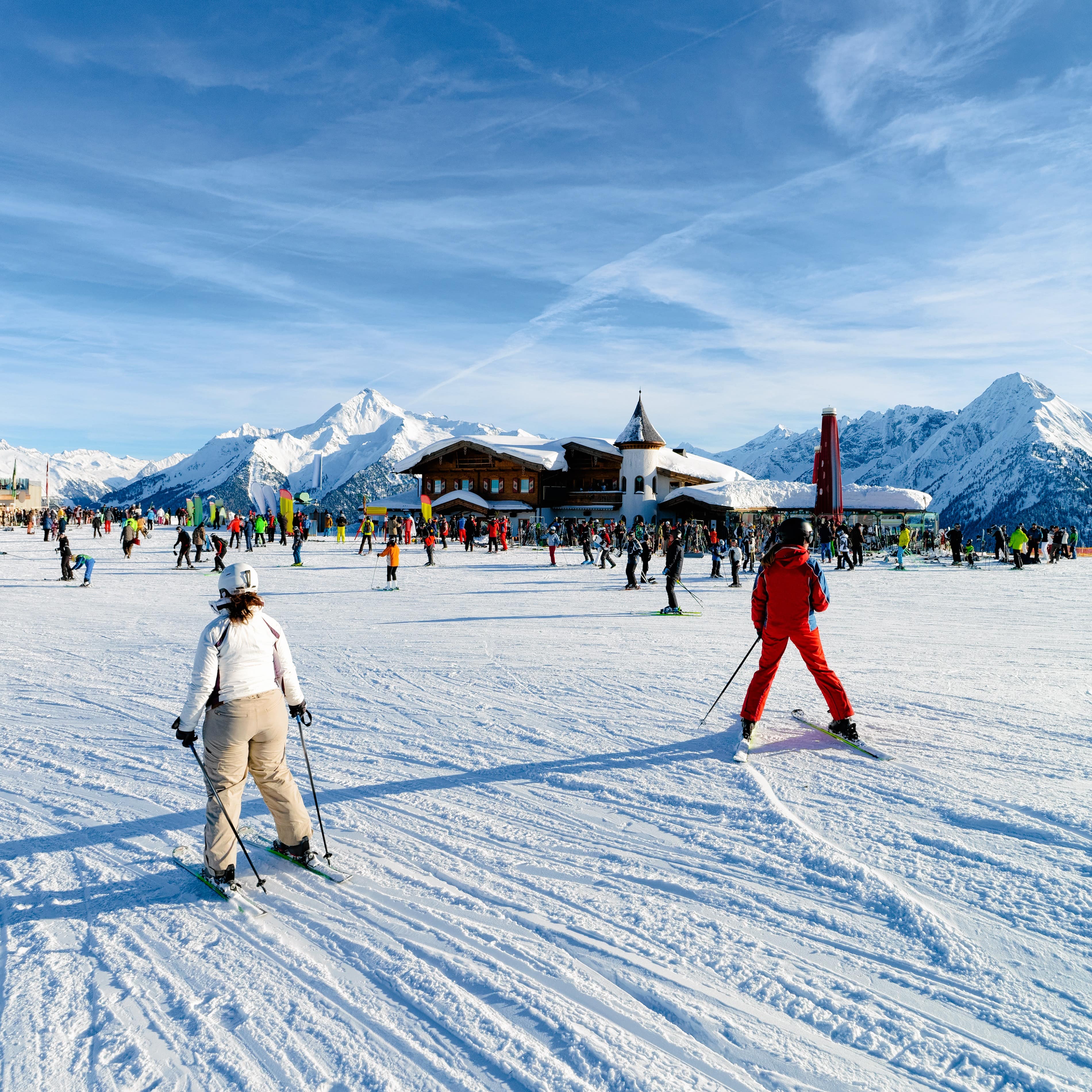 Multiple skiers enjoying the slopes and the snow covered mountains surrounding them.