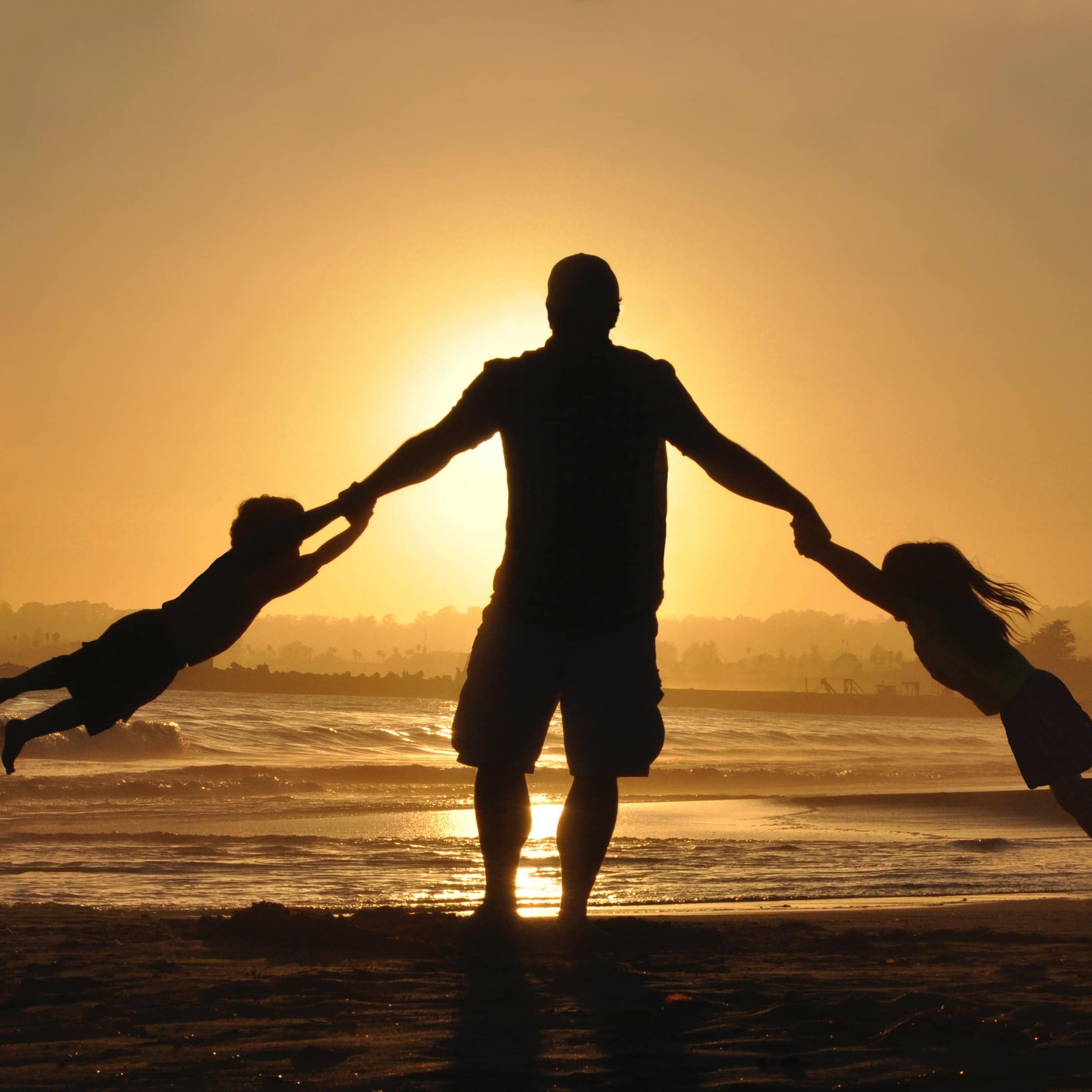Silhouette of a dad swinging his children around on a beach