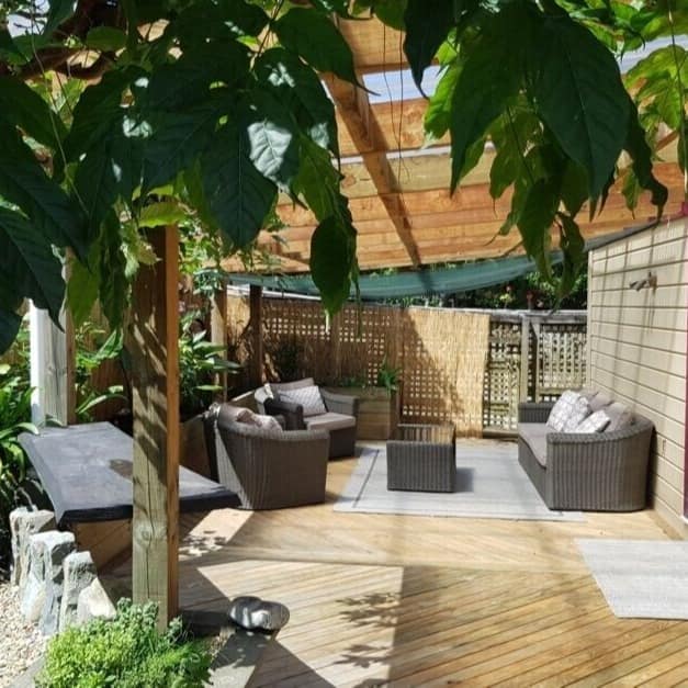 The deck of a cottage furnished with chairs with leaves hanging down in the foreground